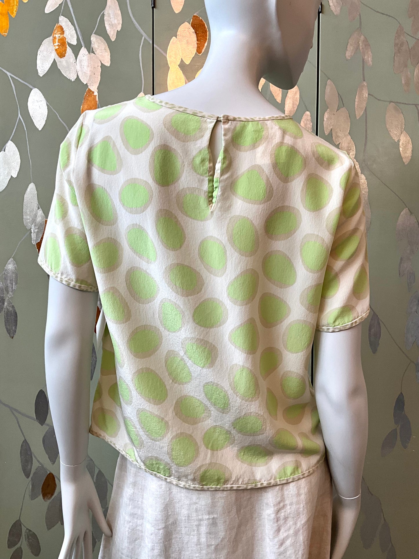 Mannequin wearing a green and white polka dot top against a patterned wall.