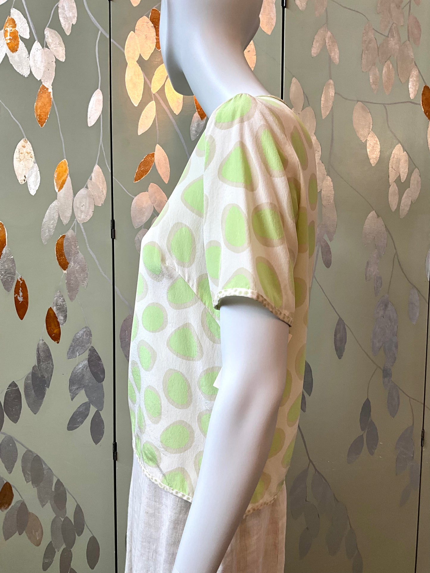 Mannequin wearing a green polka dot top against a leaf-patterned wall.
