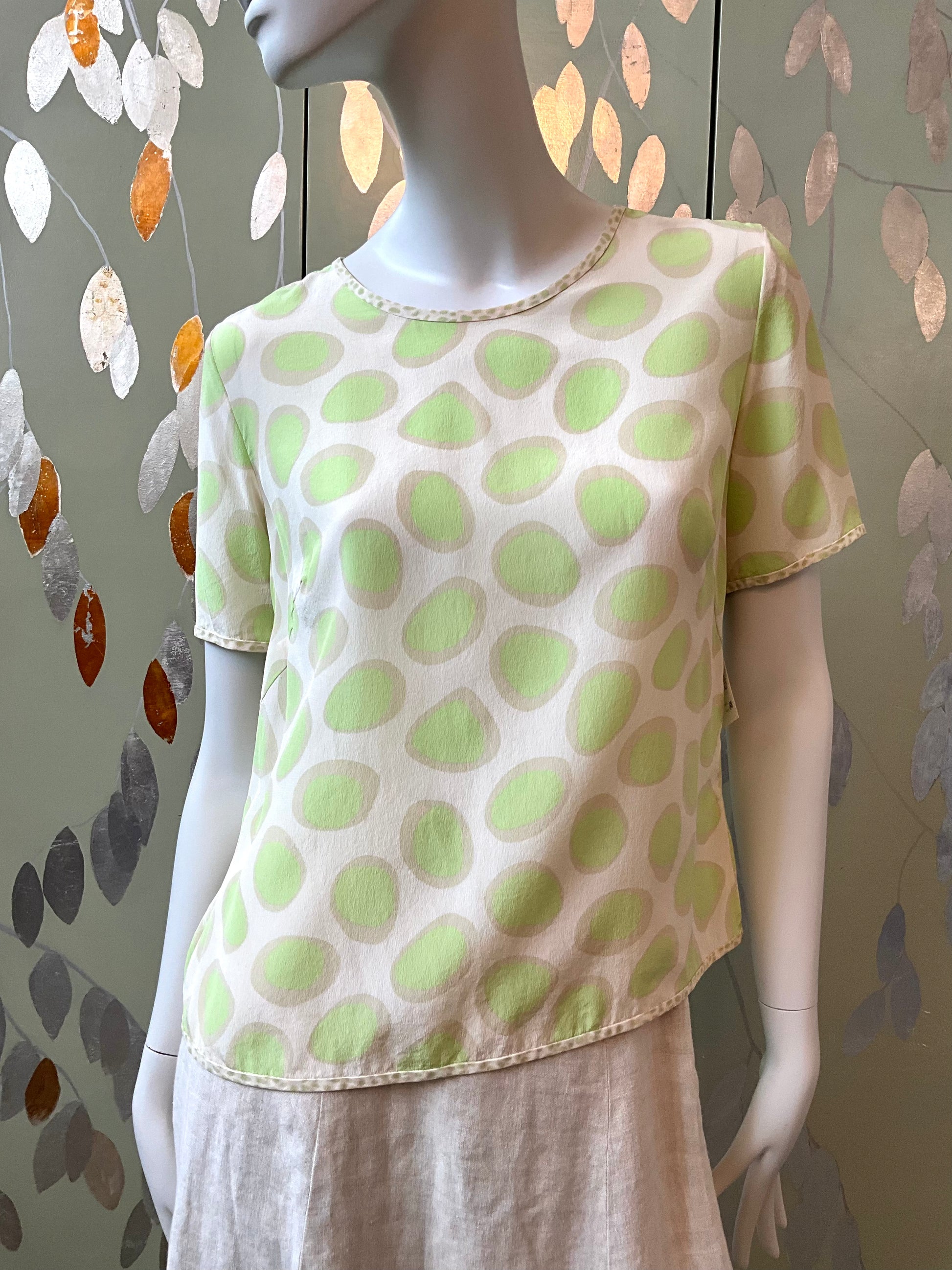 Mannequin wearing a white top with green polka dots against a decorative wall.
