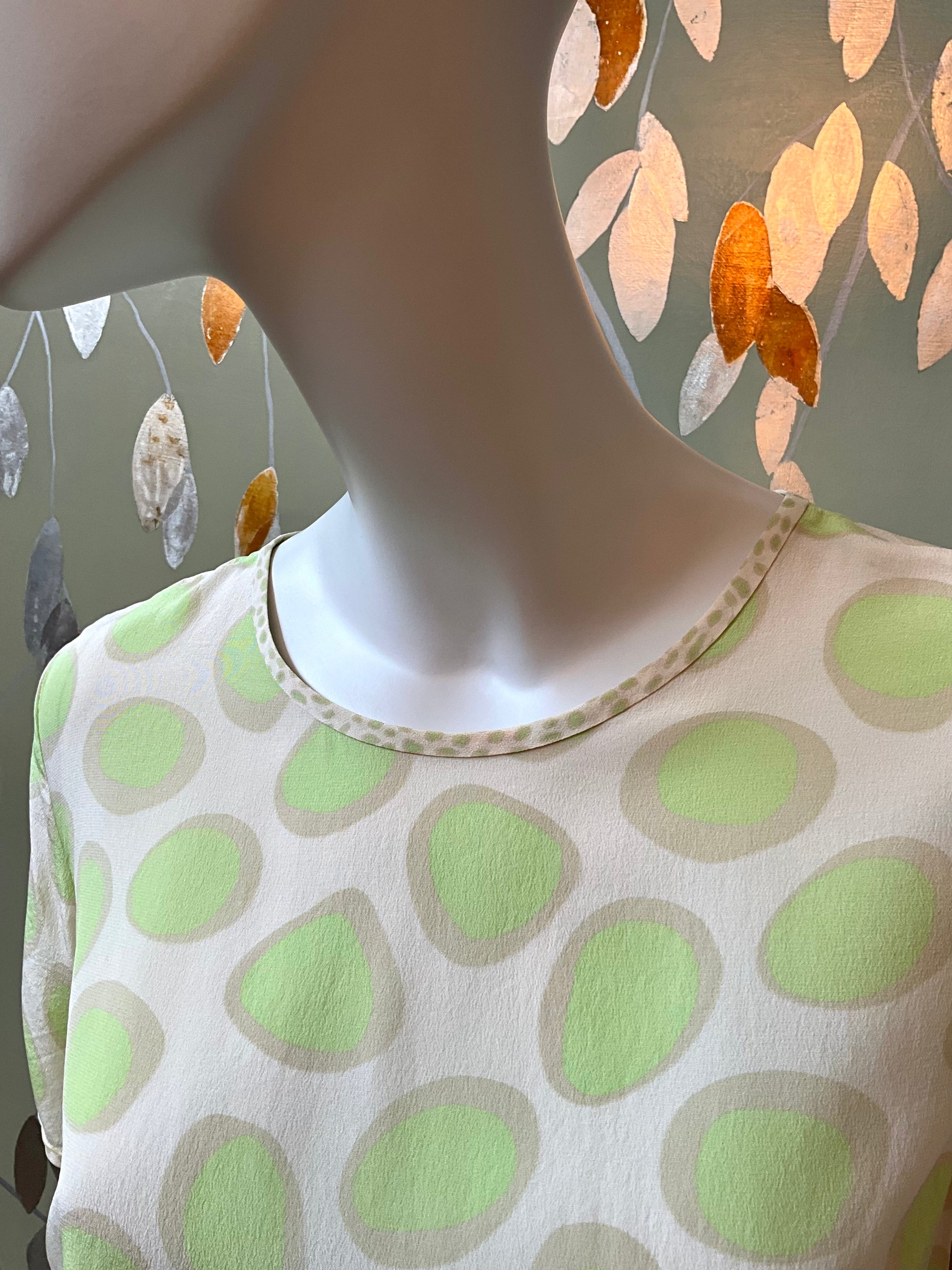 Mannequin wearing a white top with green polka dots against a neutral background