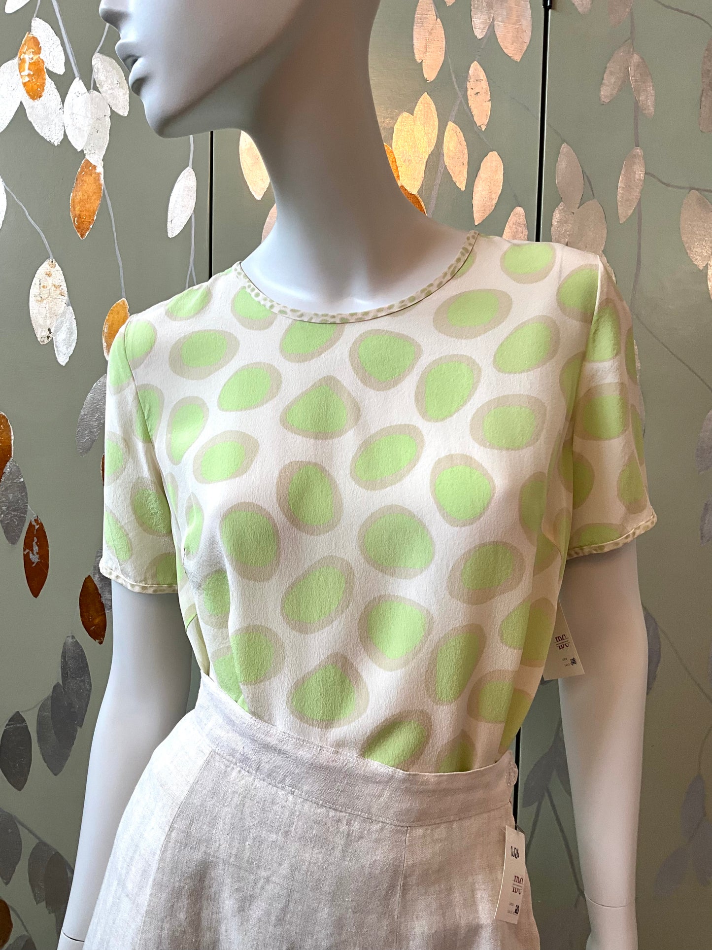 Mannequin wearing a cream top with green polka dots against a decorative wall.