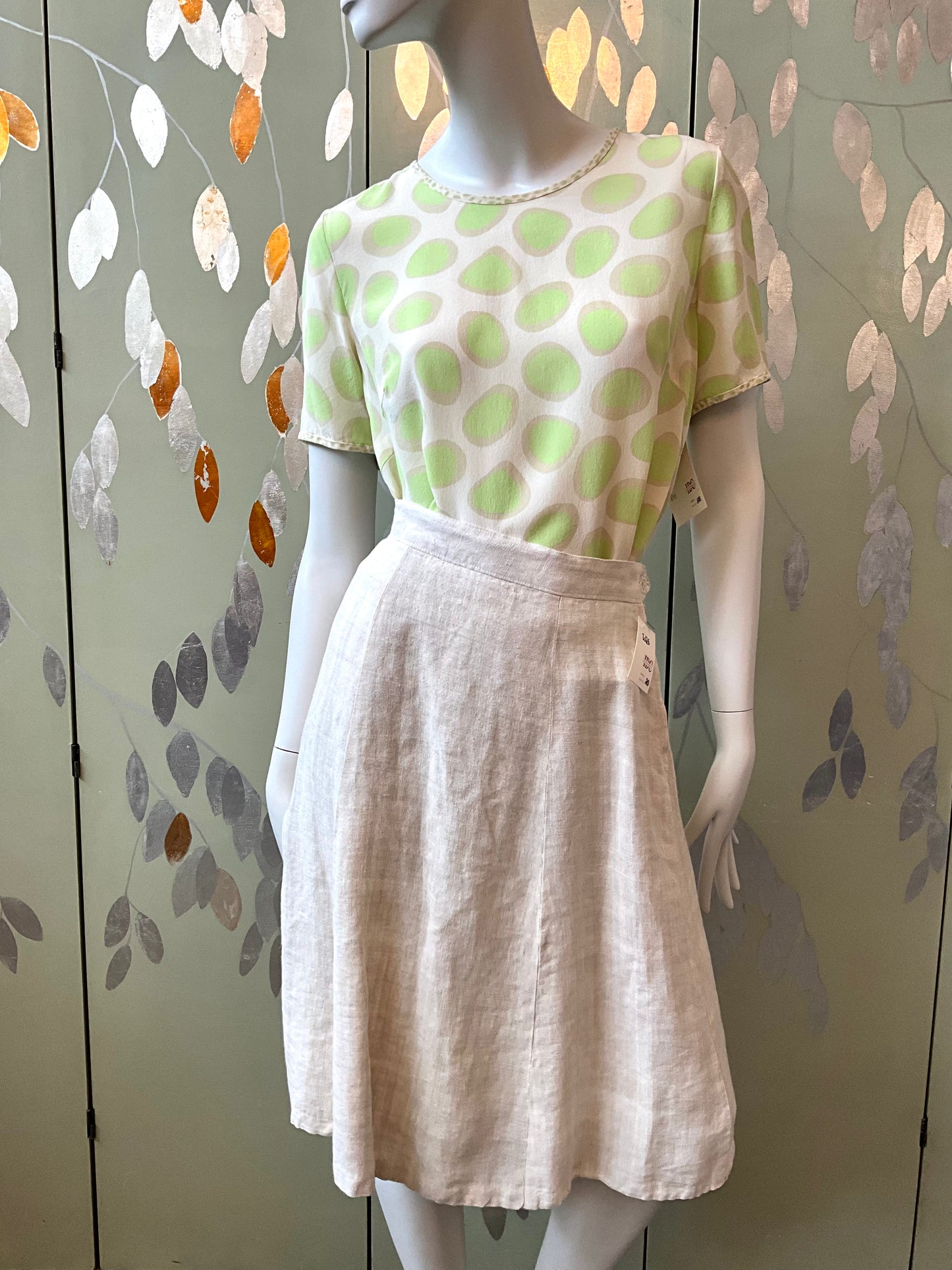 Mannequin wearing a green and white polka dot top and beige skirt against a decorative wall.