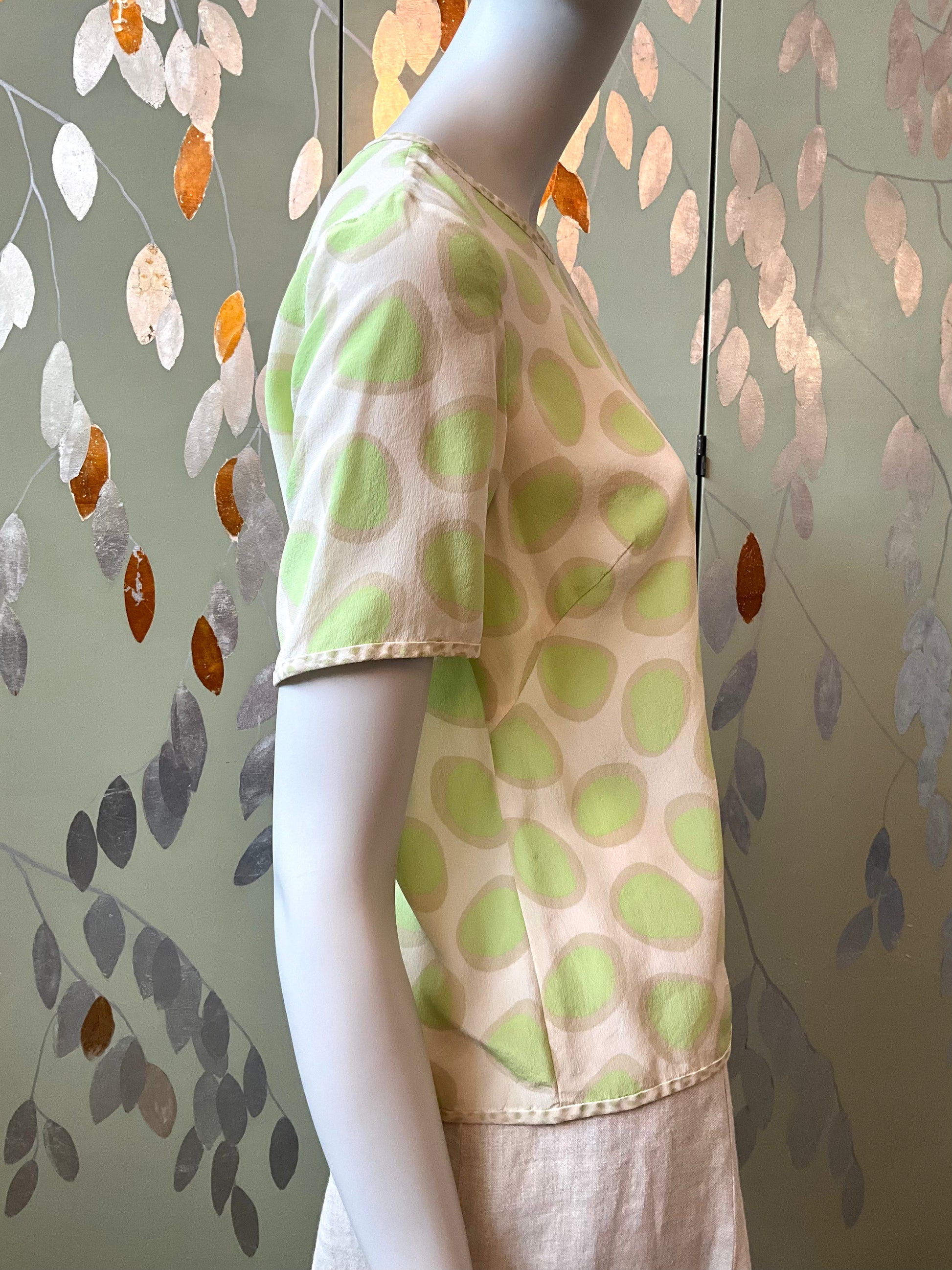 Mannequin wearing a green polka dot shirt against a leaf-patterned wall.