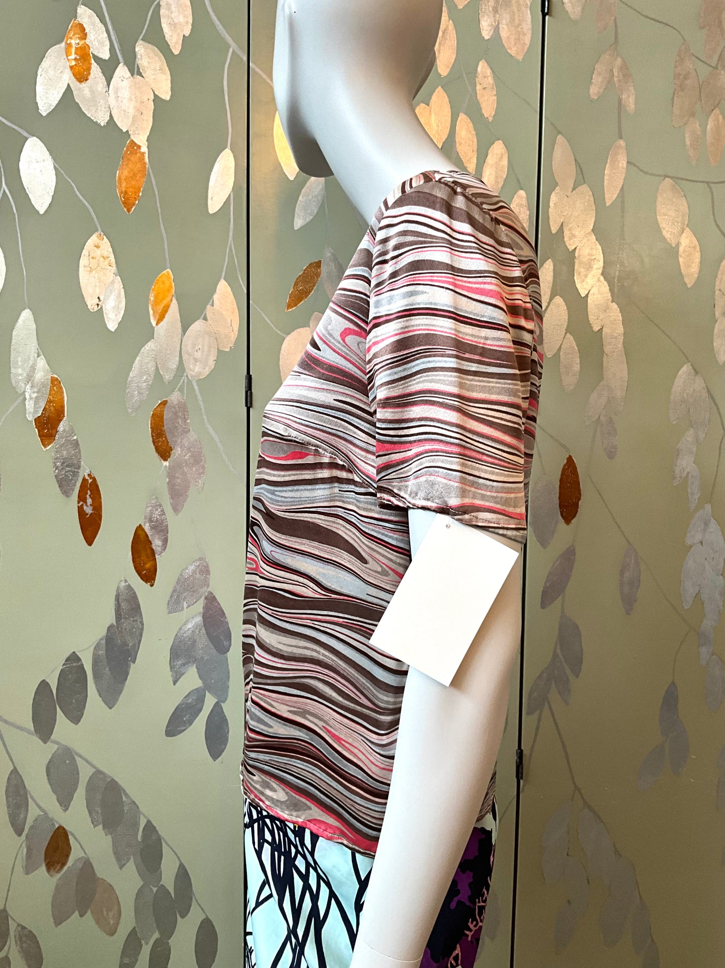 Mannequin wearing a striped top against a decorative wall with leaf patterns.