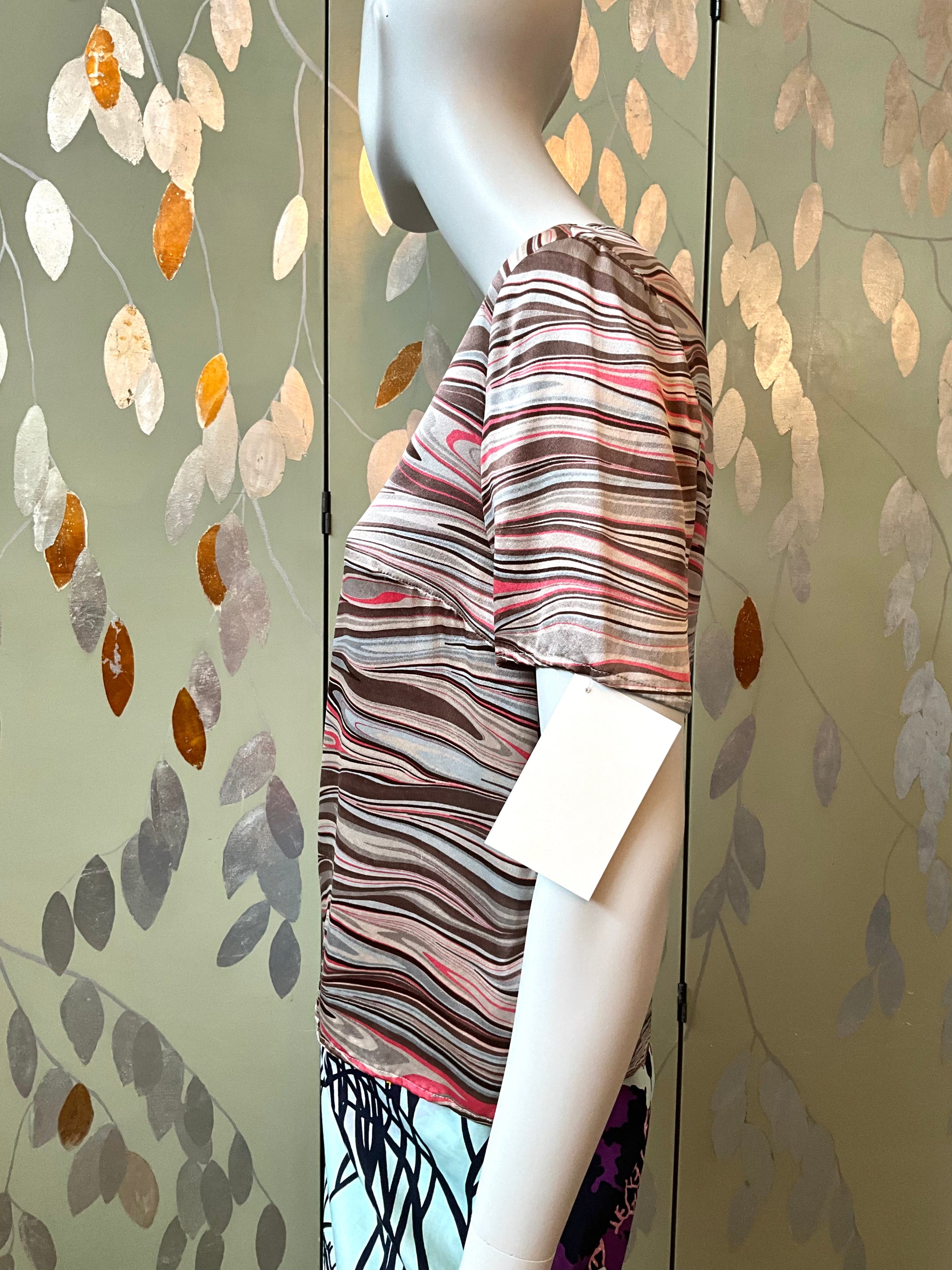 Mannequin wearing a striped top against a decorative wall with leaf patterns.