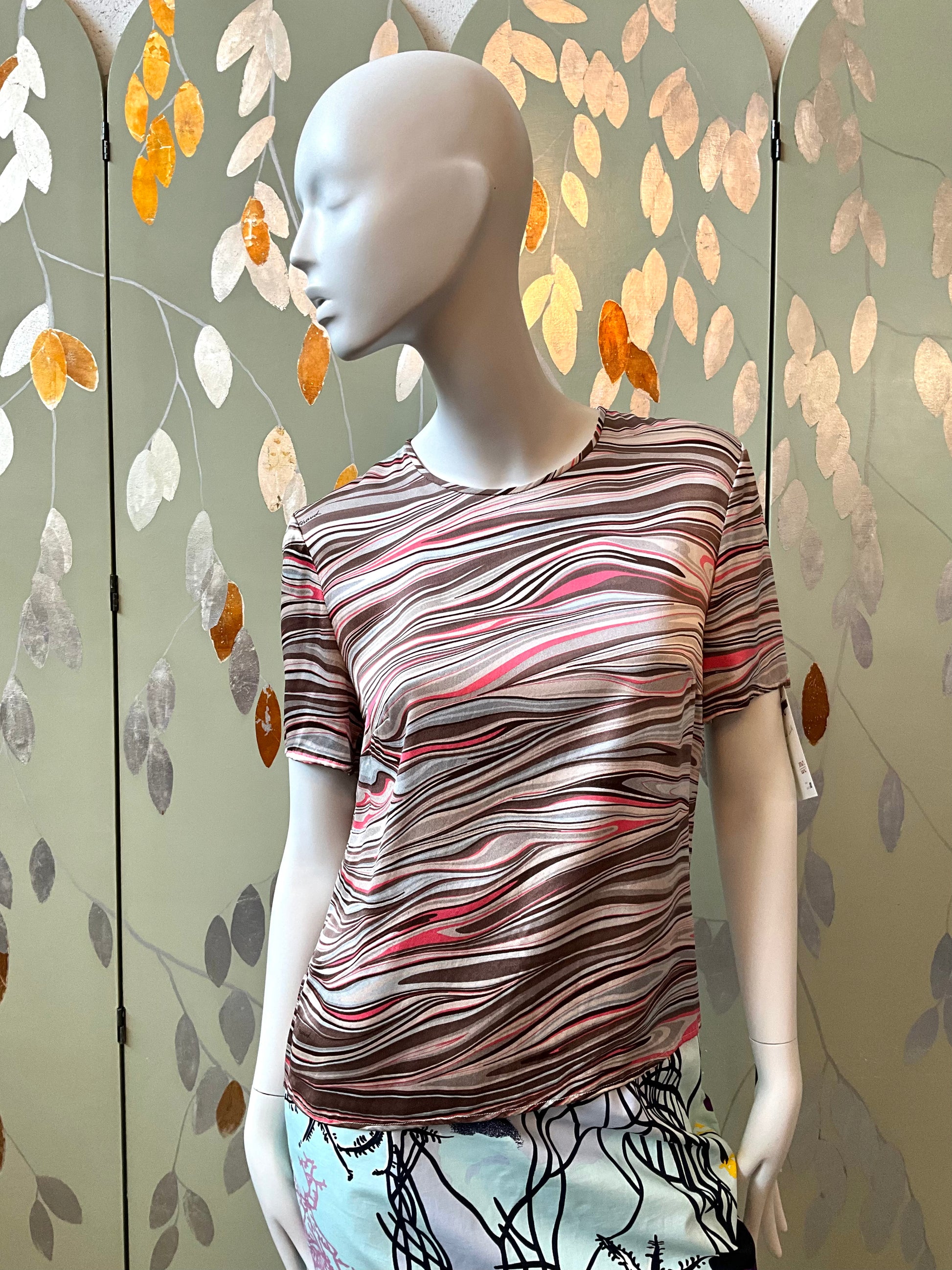 Mannequin wearing a patterned shirt against a decorative wall with leaf designs.