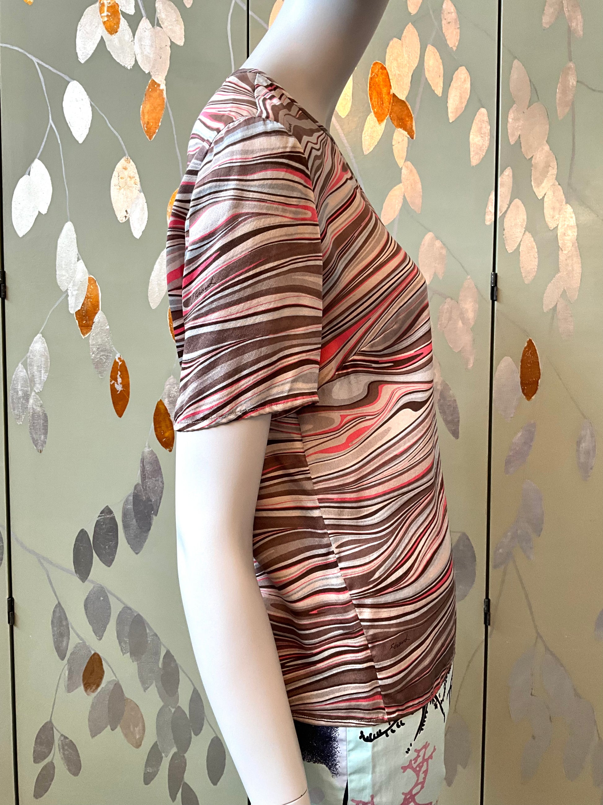 Mannequin wearing a patterned top against a decorative wall with leaf designs.