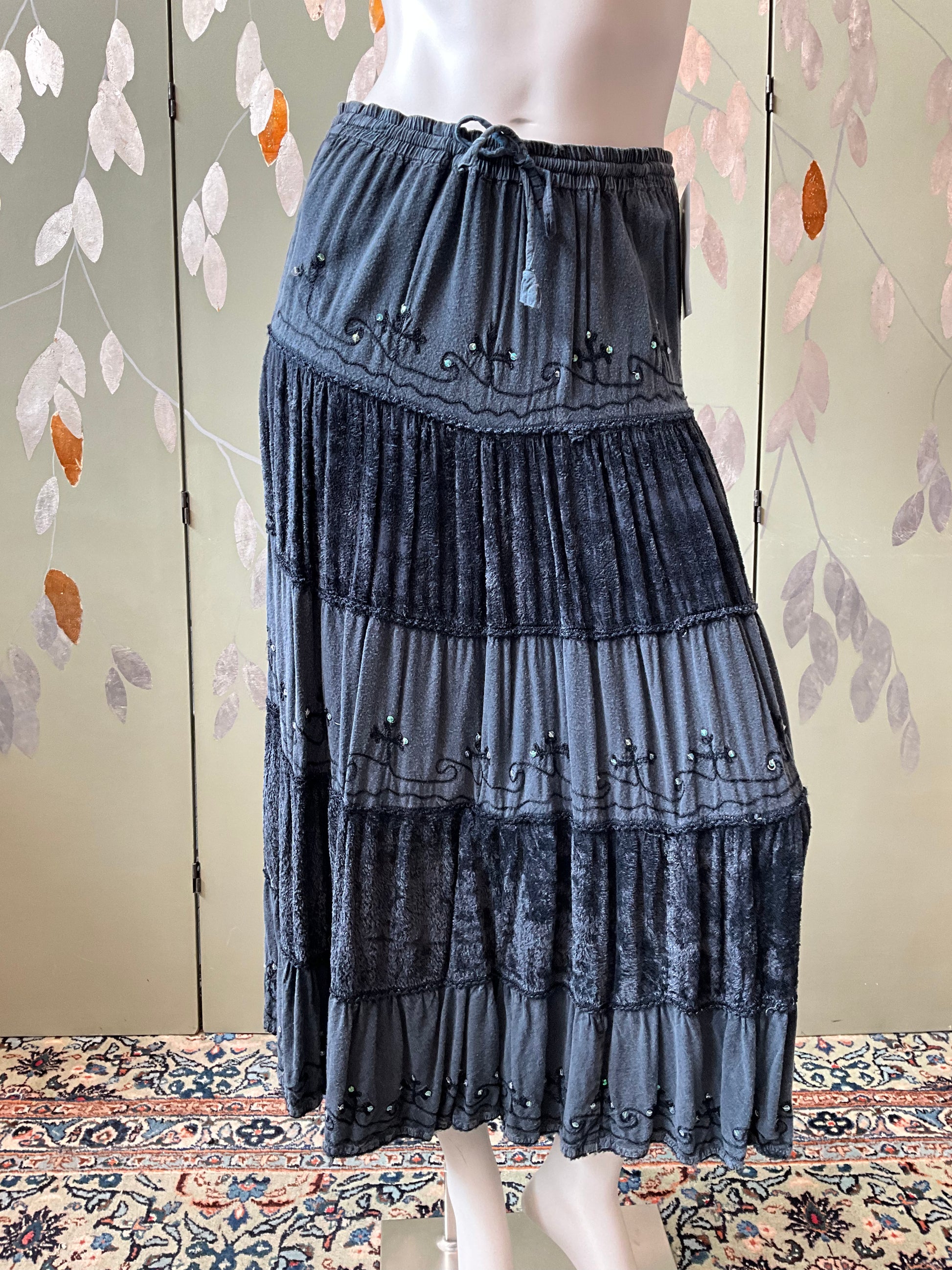 Long grey skirt with layered design on a mannequin against a floral-patterned wall.