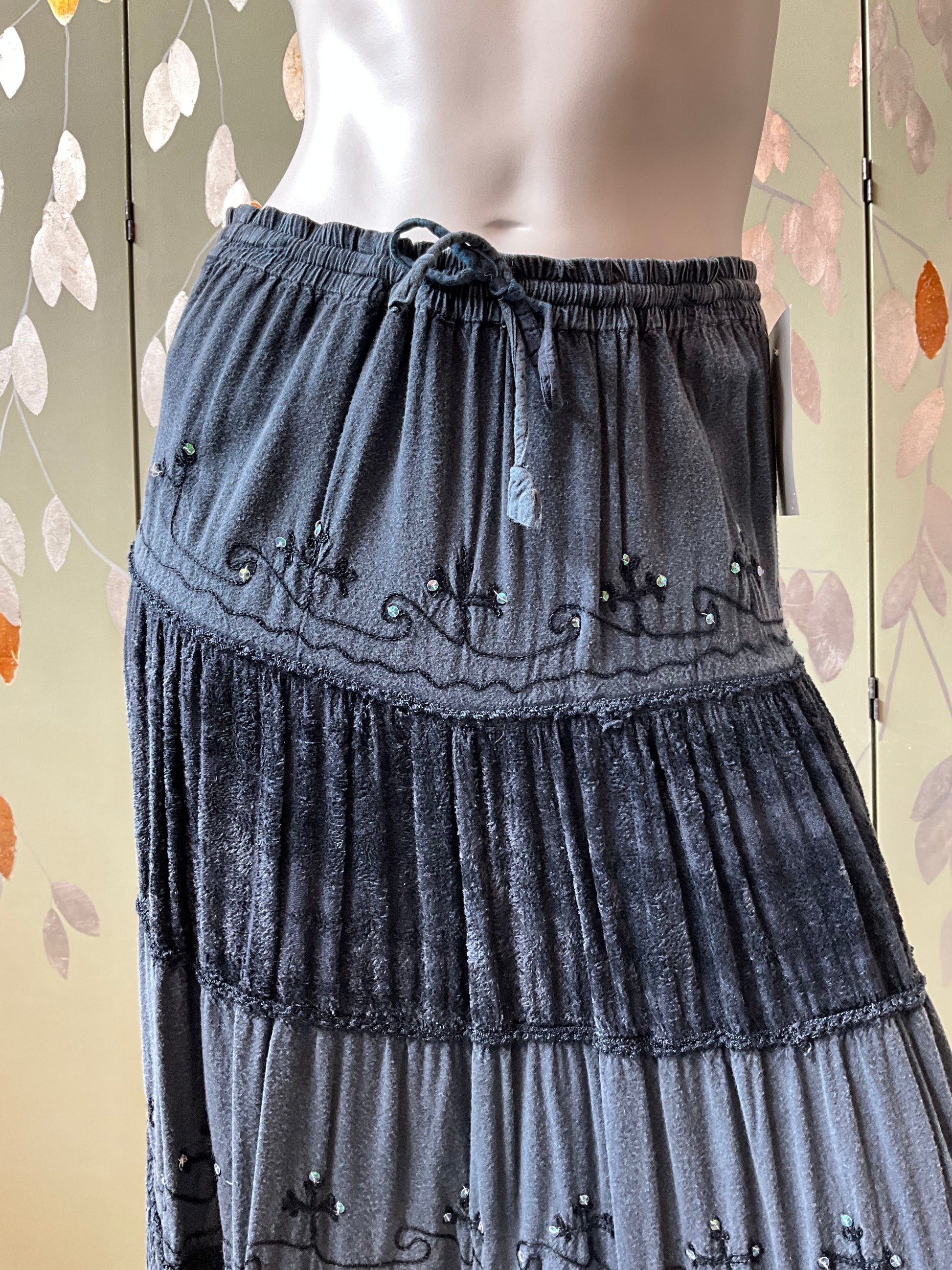 Gray tiered skirt with decorative elements on a mannequin against a floral background