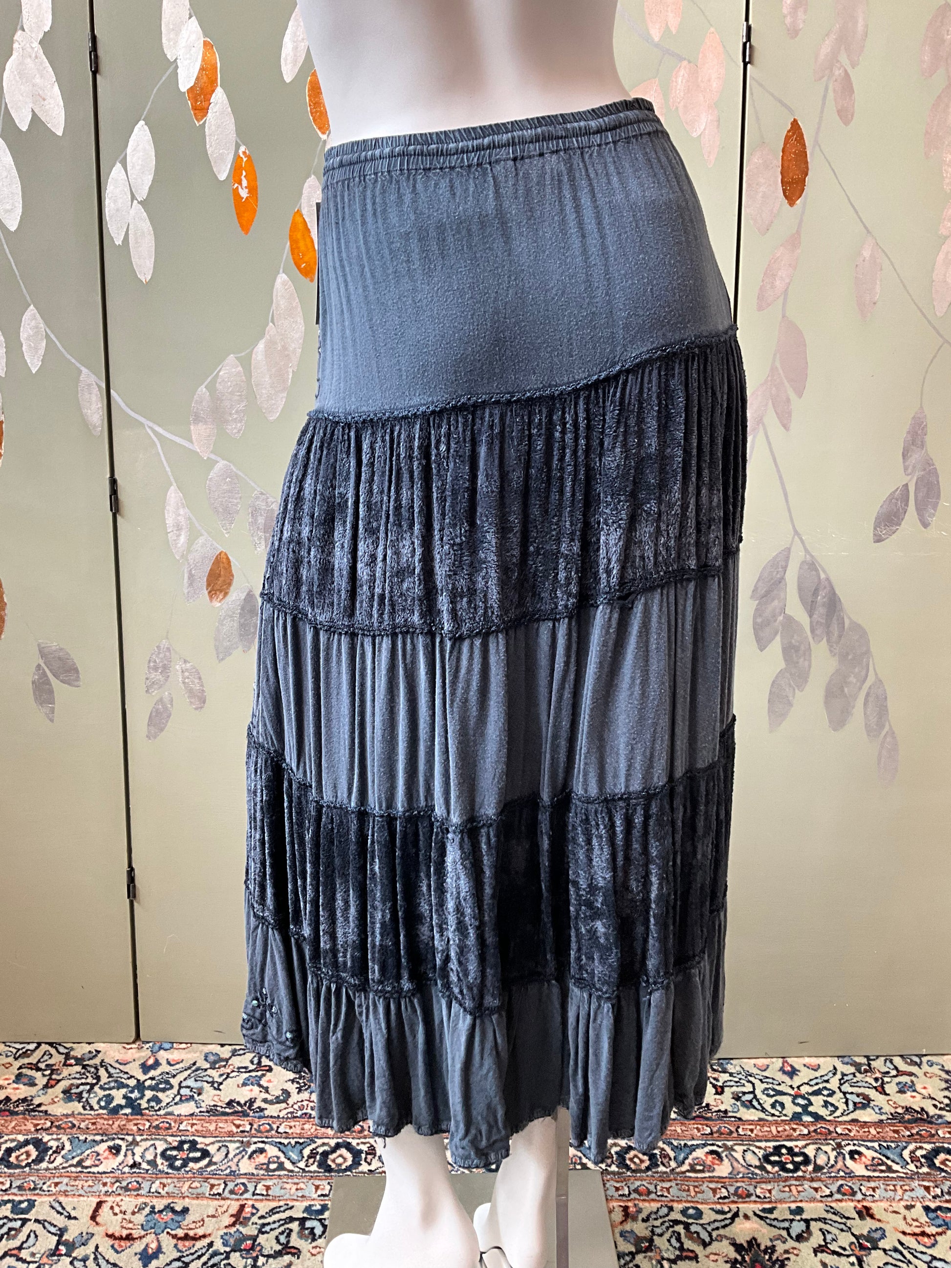 Mannequin wearing a tiered grey skirt against a floral-patterned wall.