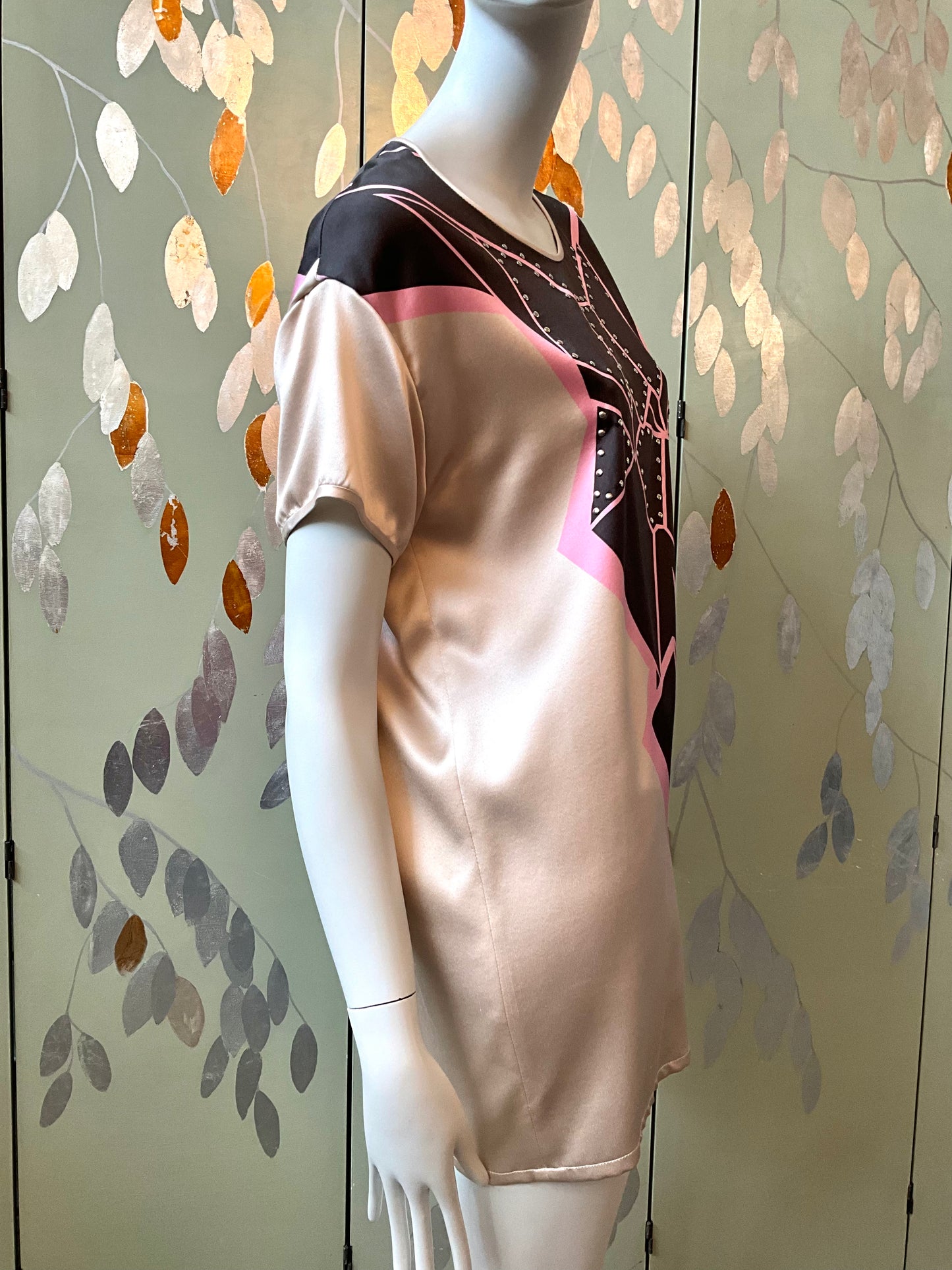 Mannequin wearing a beige top with a geometric pattern against a decorative wall.