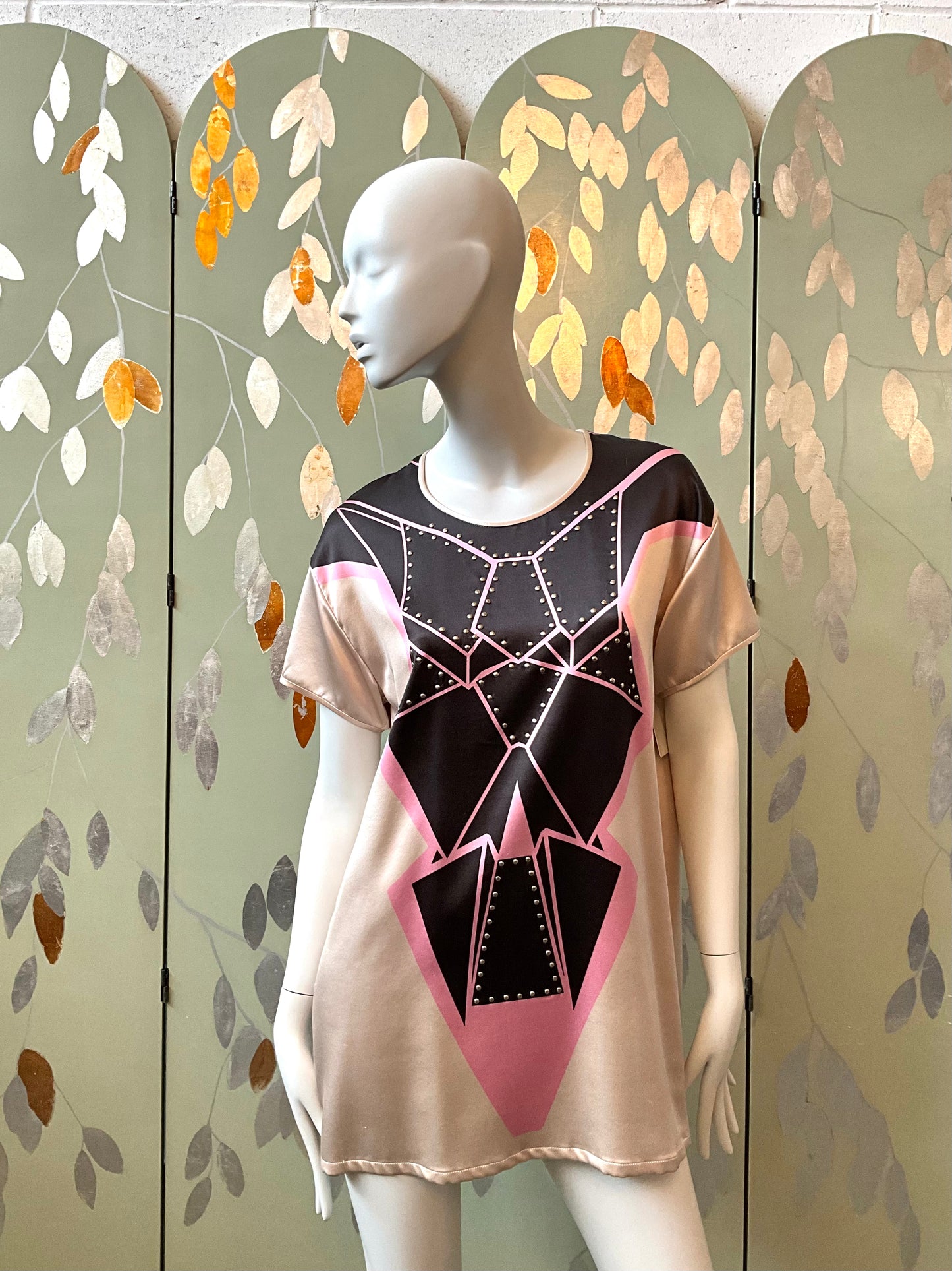 Mannequin wearing a black and pink geometric-patterned top against a decorative screen.