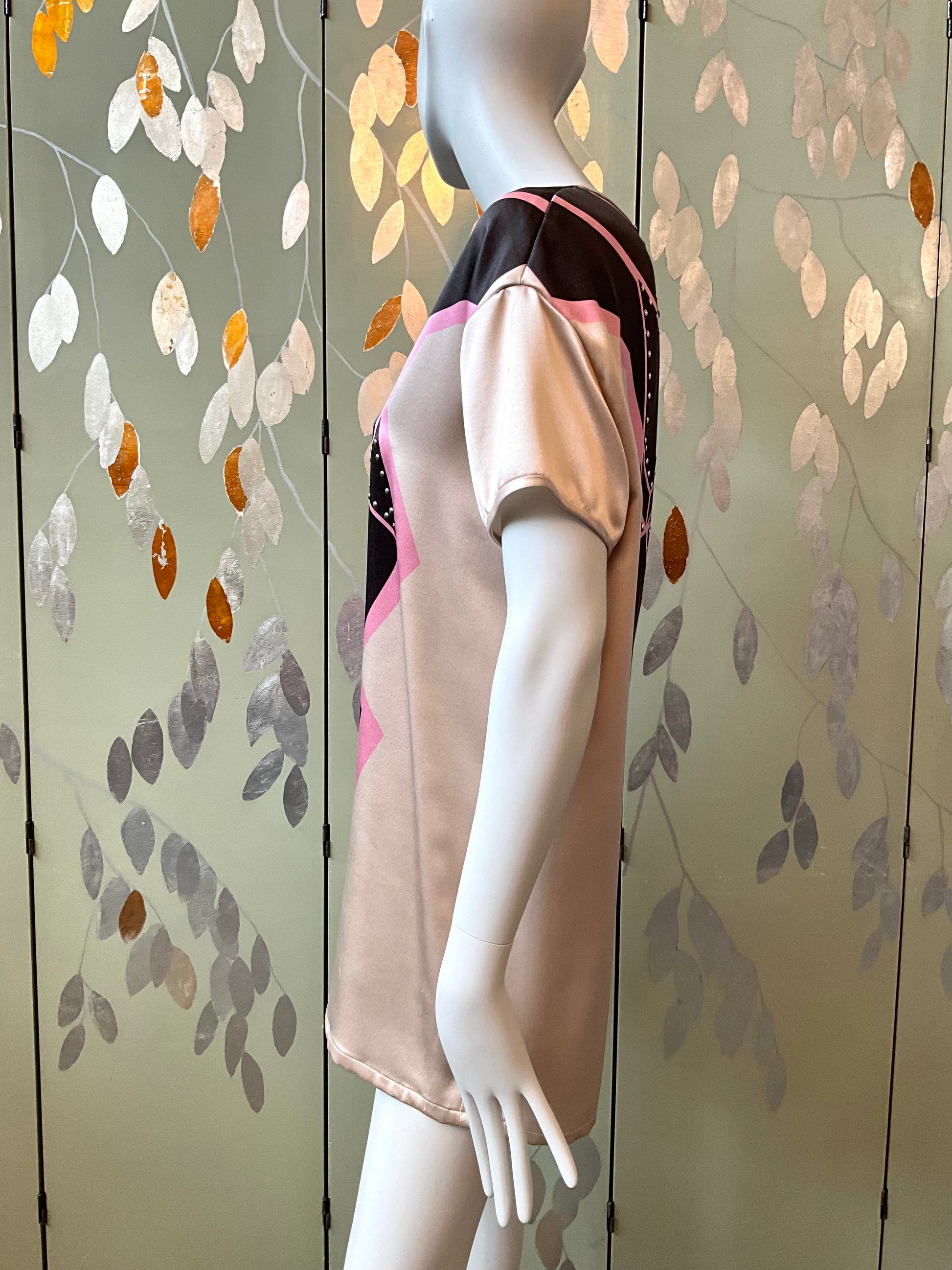 Mannequin wearing a beige top with pink accents against a decorative wall.