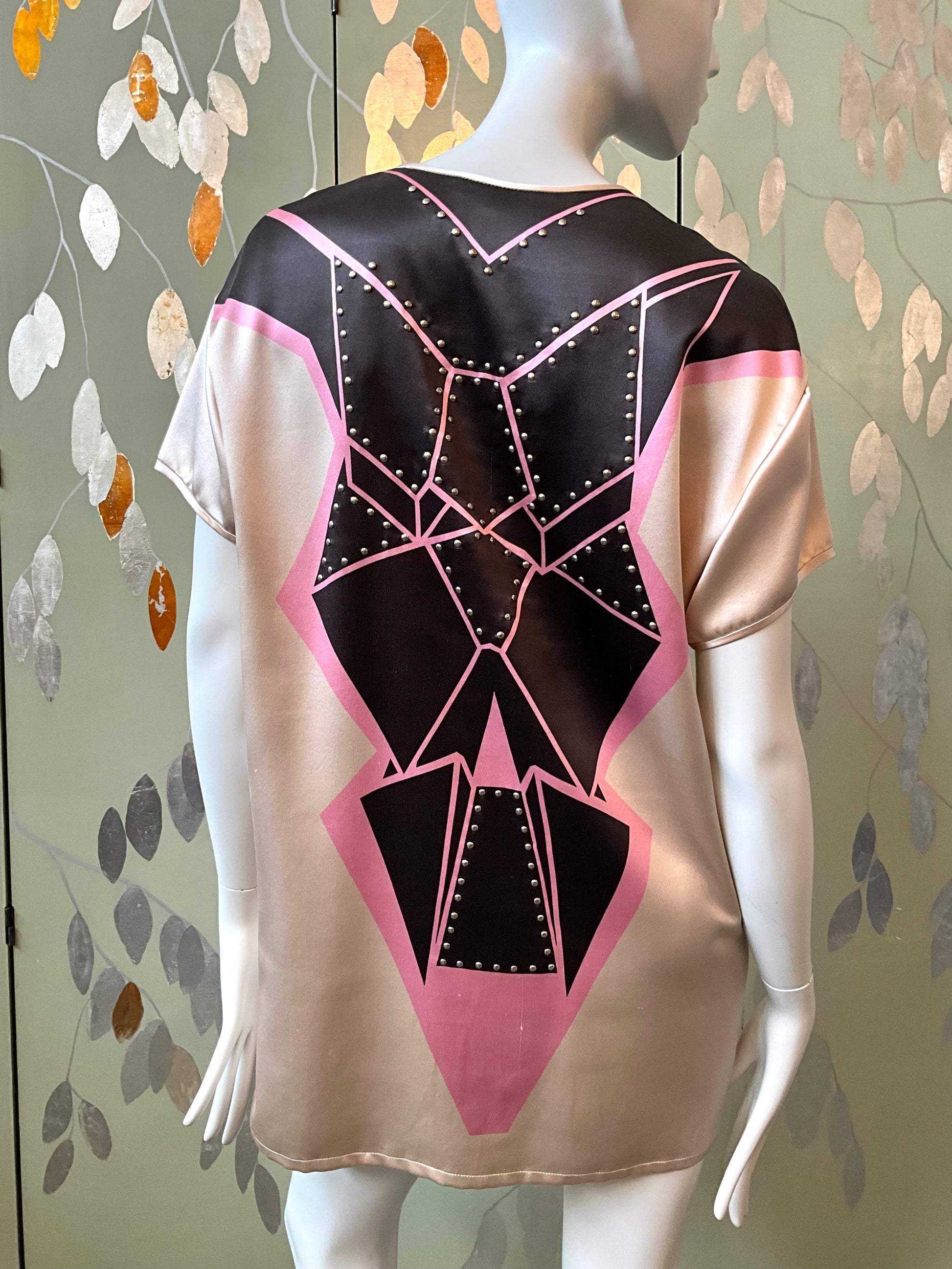 Mannequin wearing a black and pink geometric-patterned top against a decorative wall.