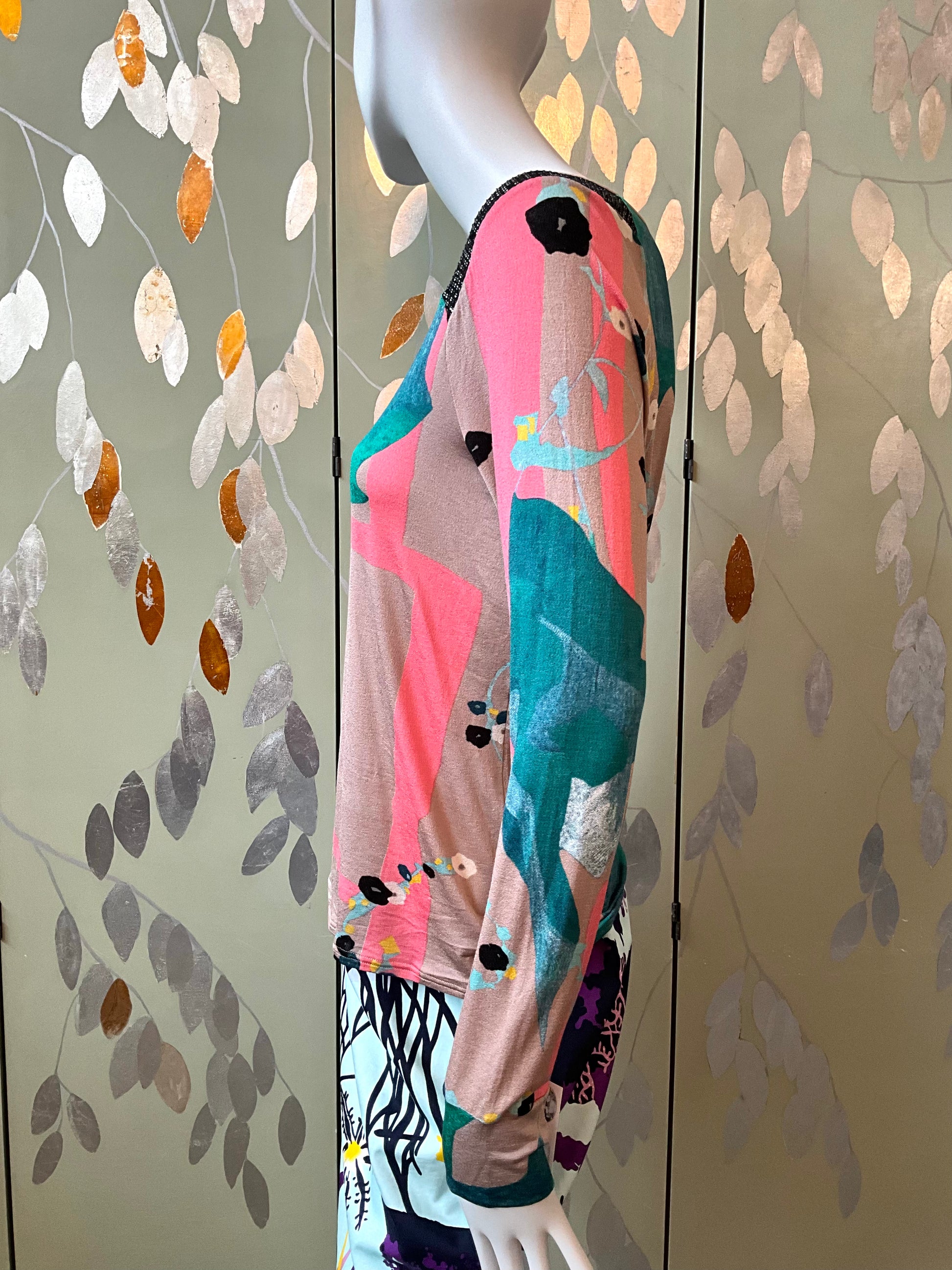 Mannequin wearing a colorful top with abstract patterns against a leaf-patterned wall.