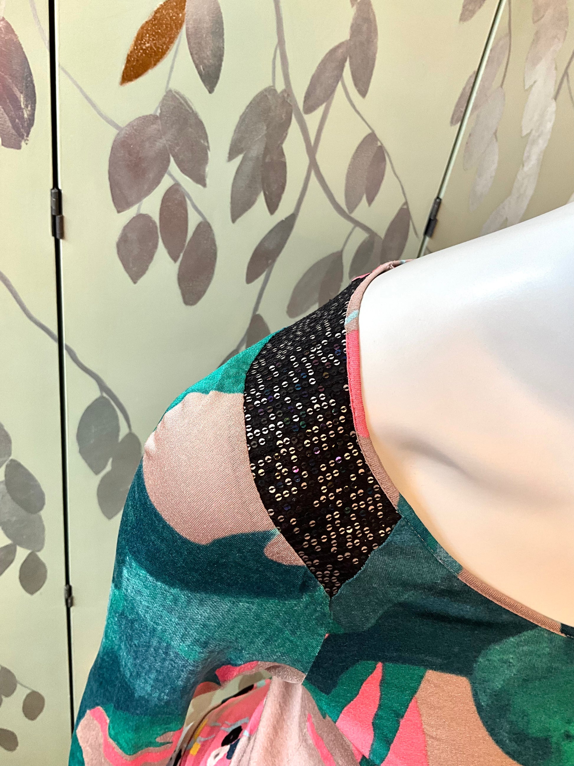Close-up of a mannequin  wearing a colorful sequin top with abstract patterns against a patterned wall.