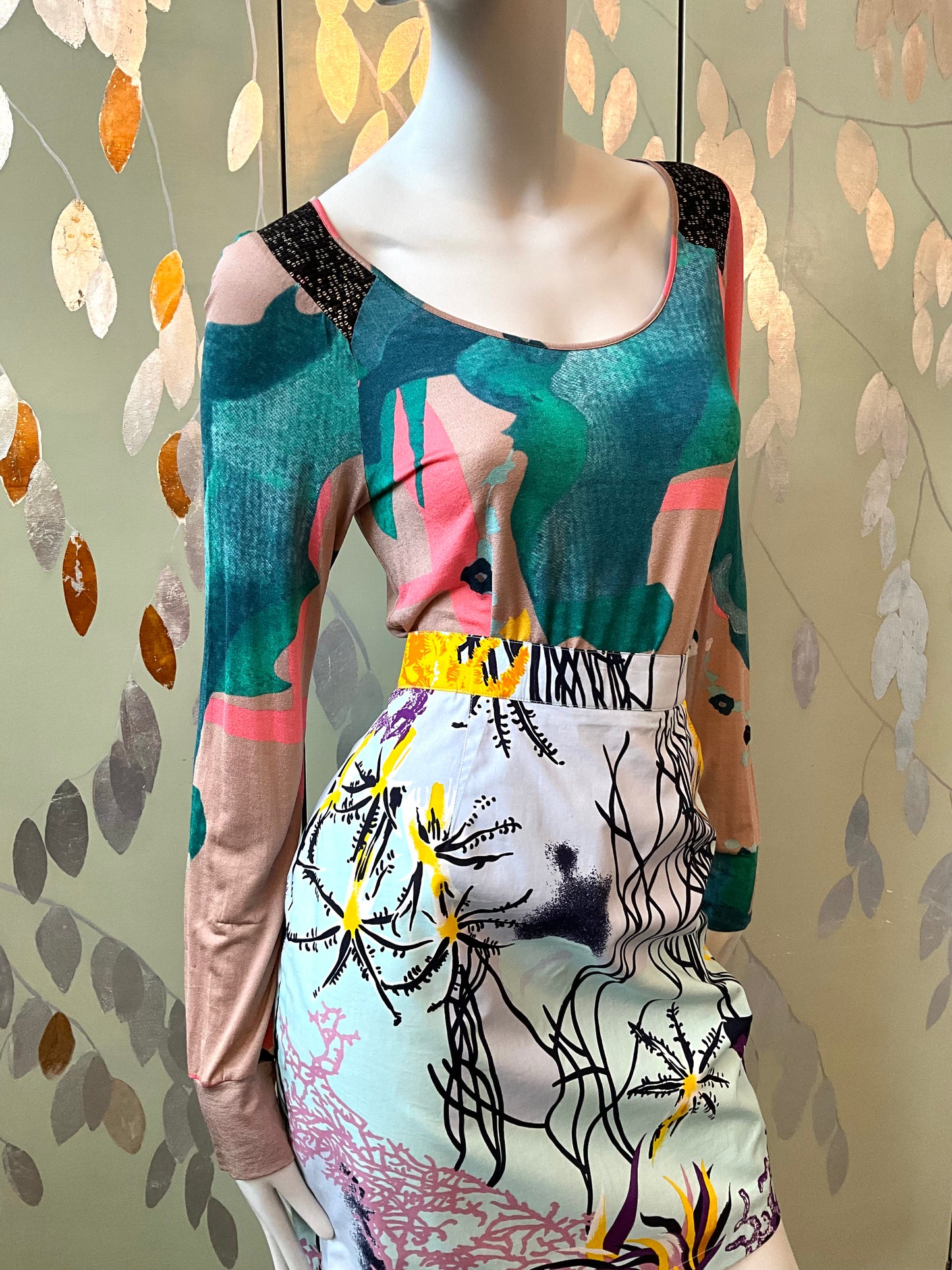 Mannequin wearing a colorful top with abstract patterns against a leafy background