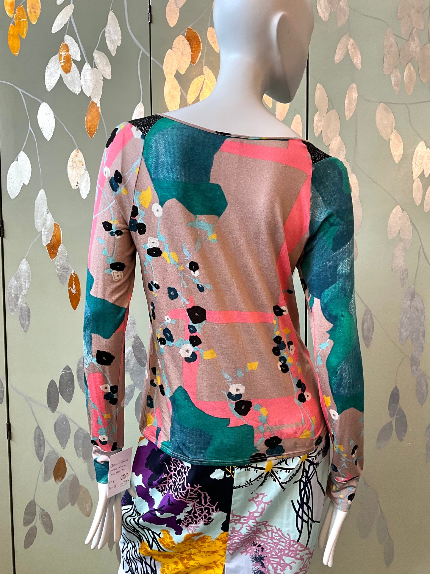 Mannequin wearing a colorful abstract patterned top against a decorative wall.