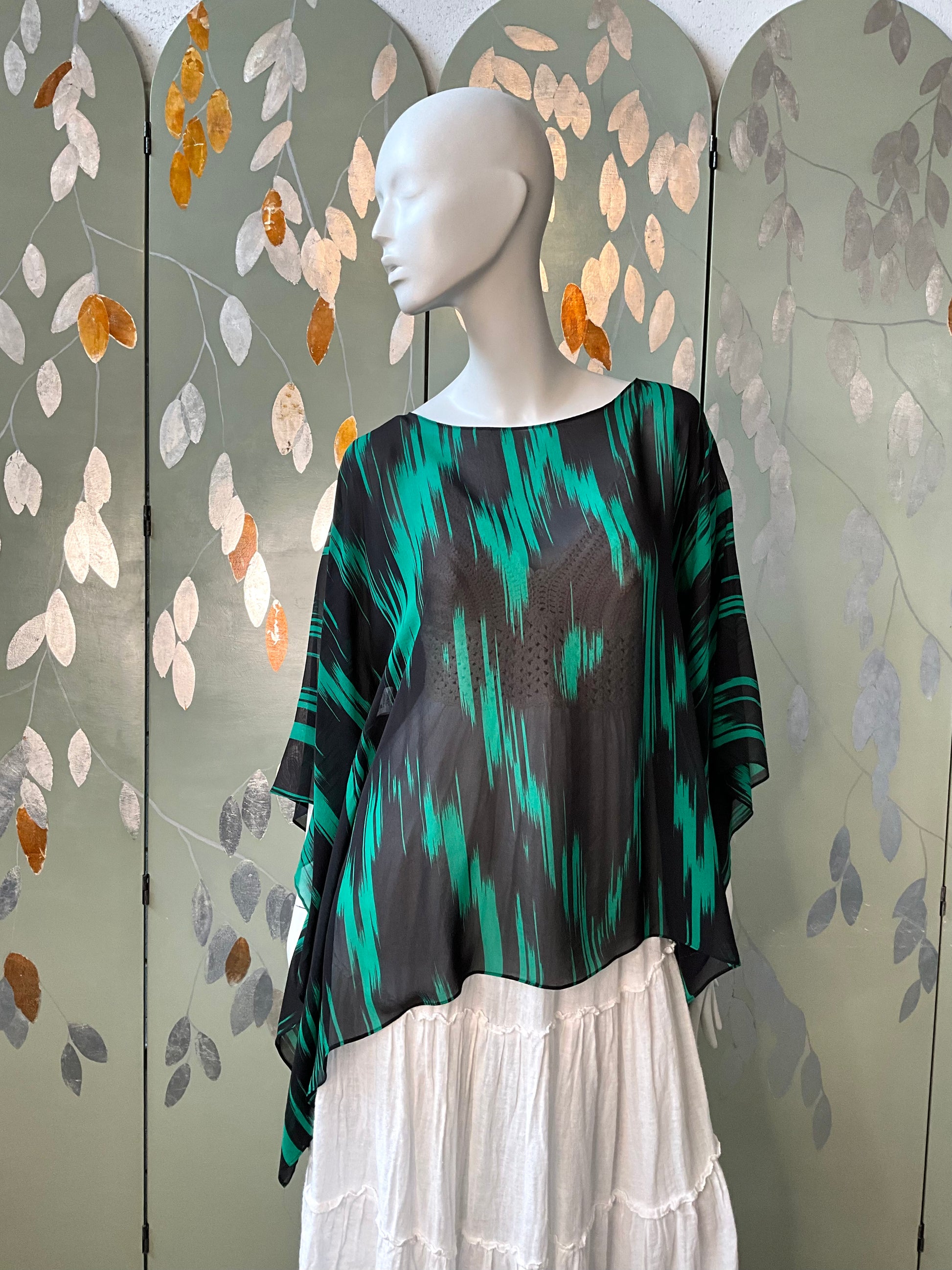 Mannequin wearing a green and black patterned top with a white skirt against a decorative wall.