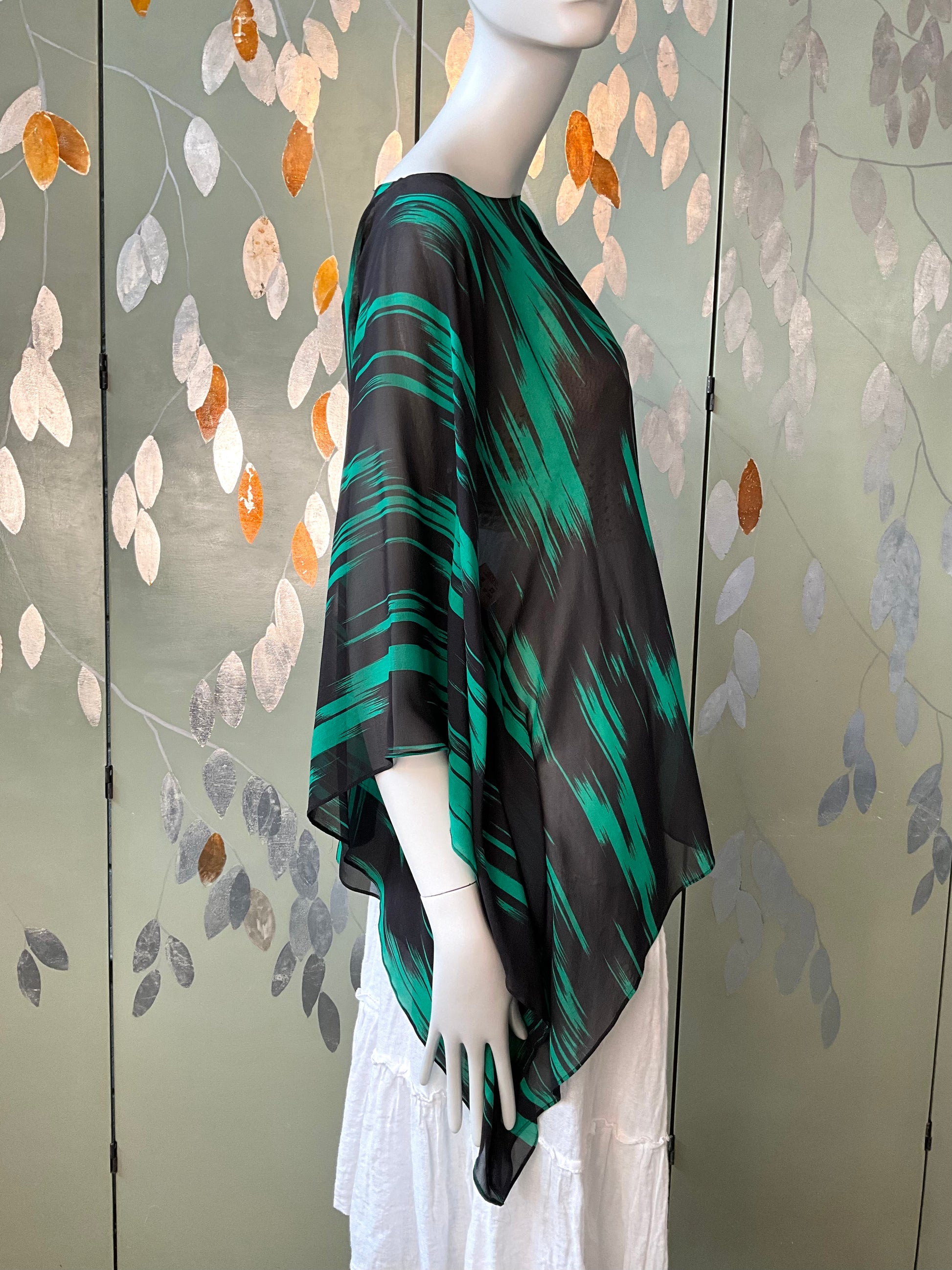 Mannequin wearing a green and black patterned top against a decorative wall.