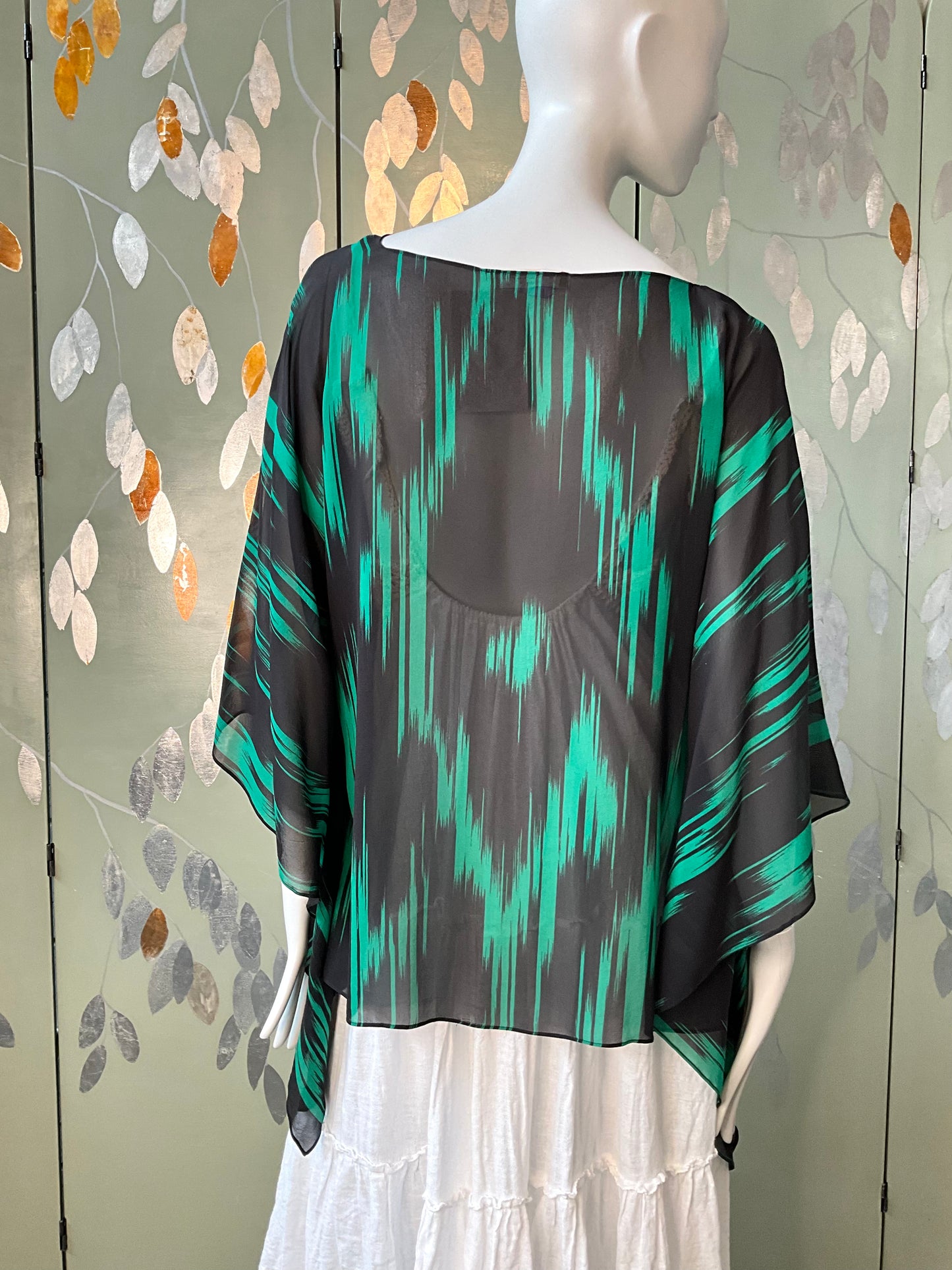 Mannequin wearing a black and green patterned top with a white skirt against a decorative wall.