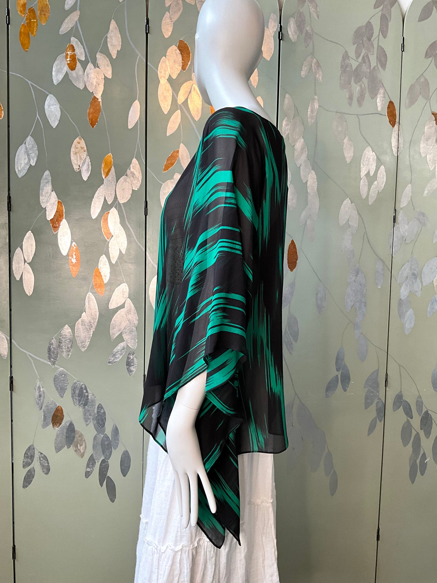 Mannequin wearing a black and green patterned top against a decorative wall.