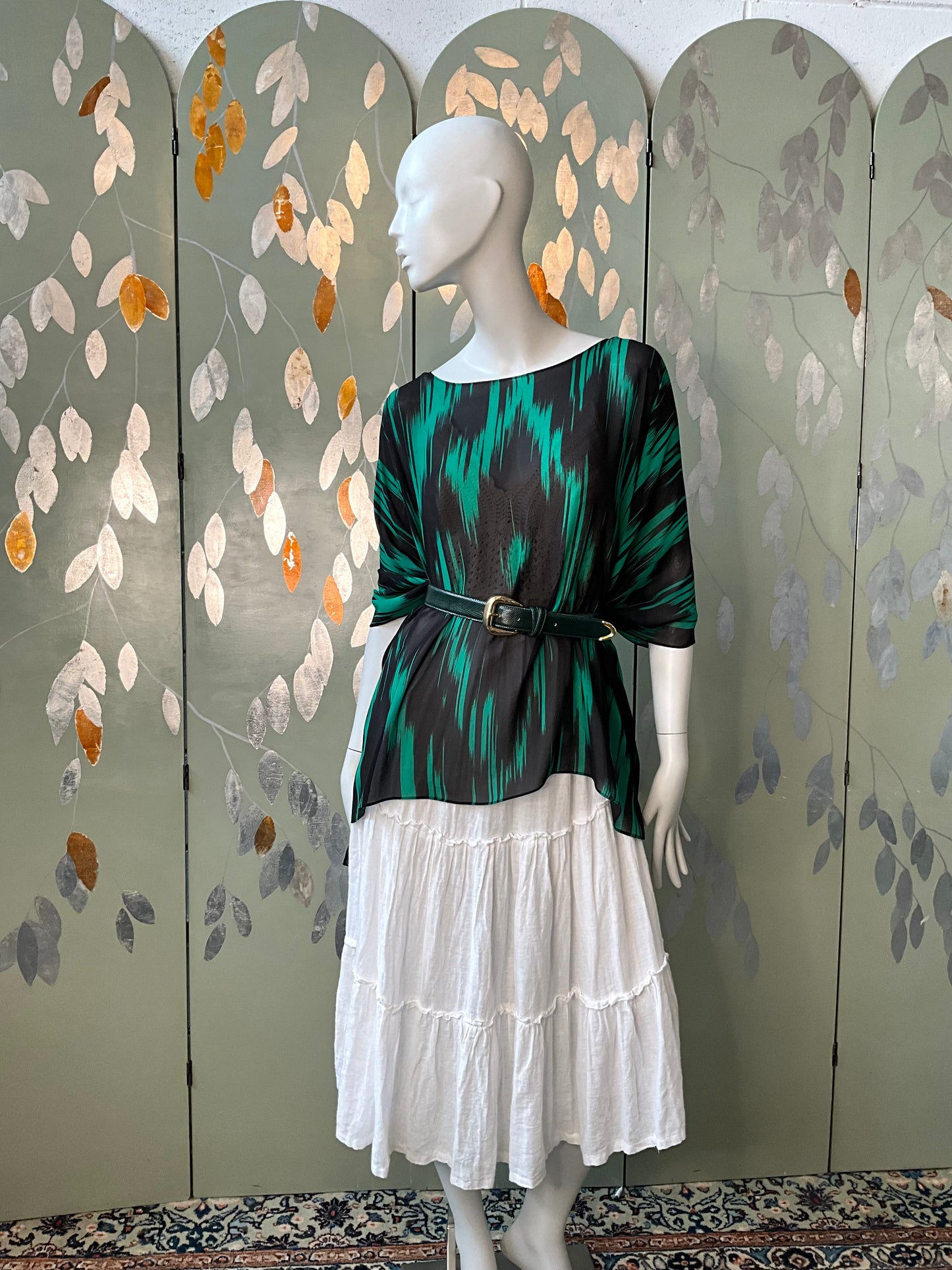 Mannequin wearing a green and black top with a white skirt against a decorative wall.