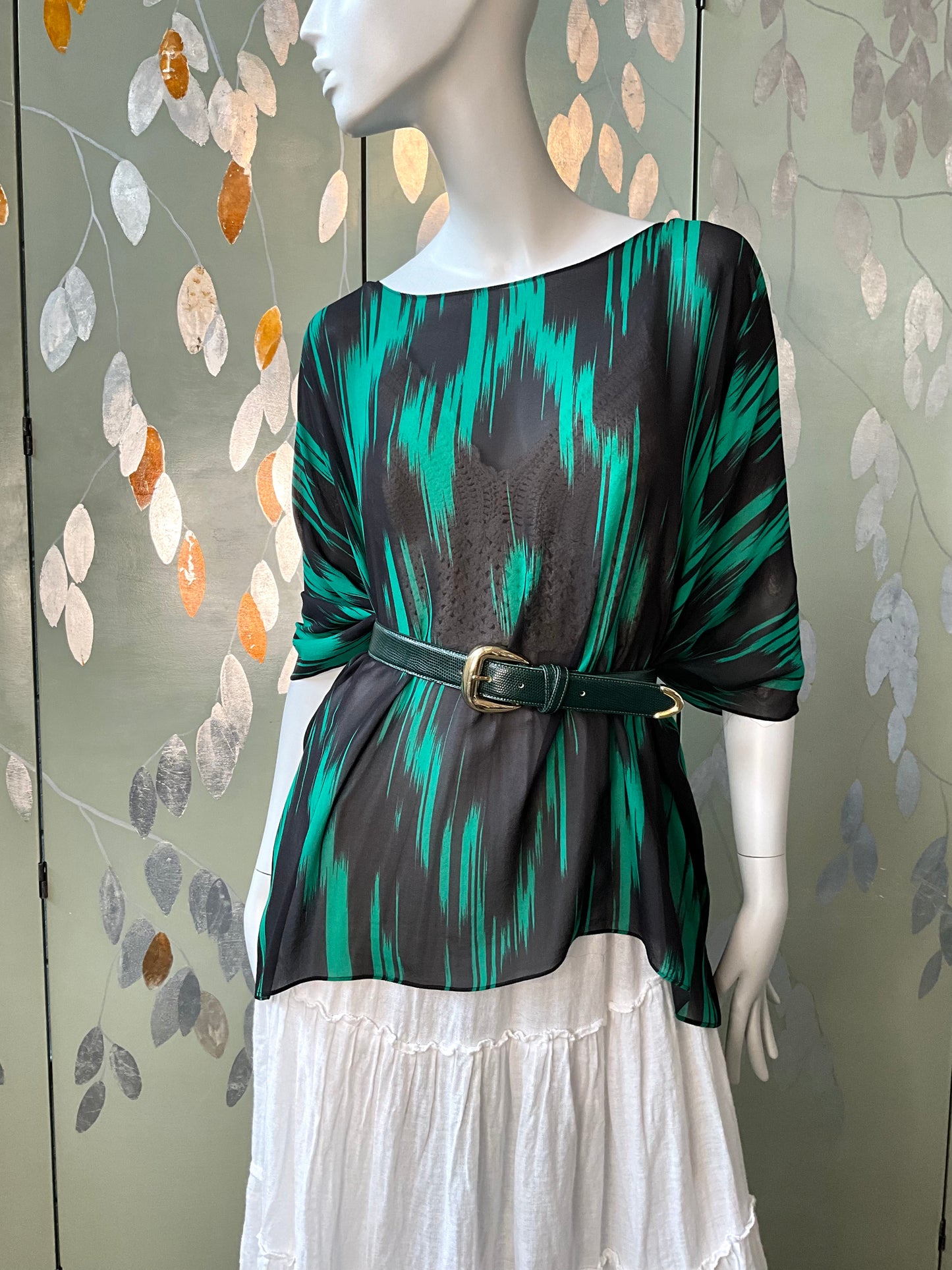 Mannequin wearing a green and black patterned top with a white skirt against a decorative wall.