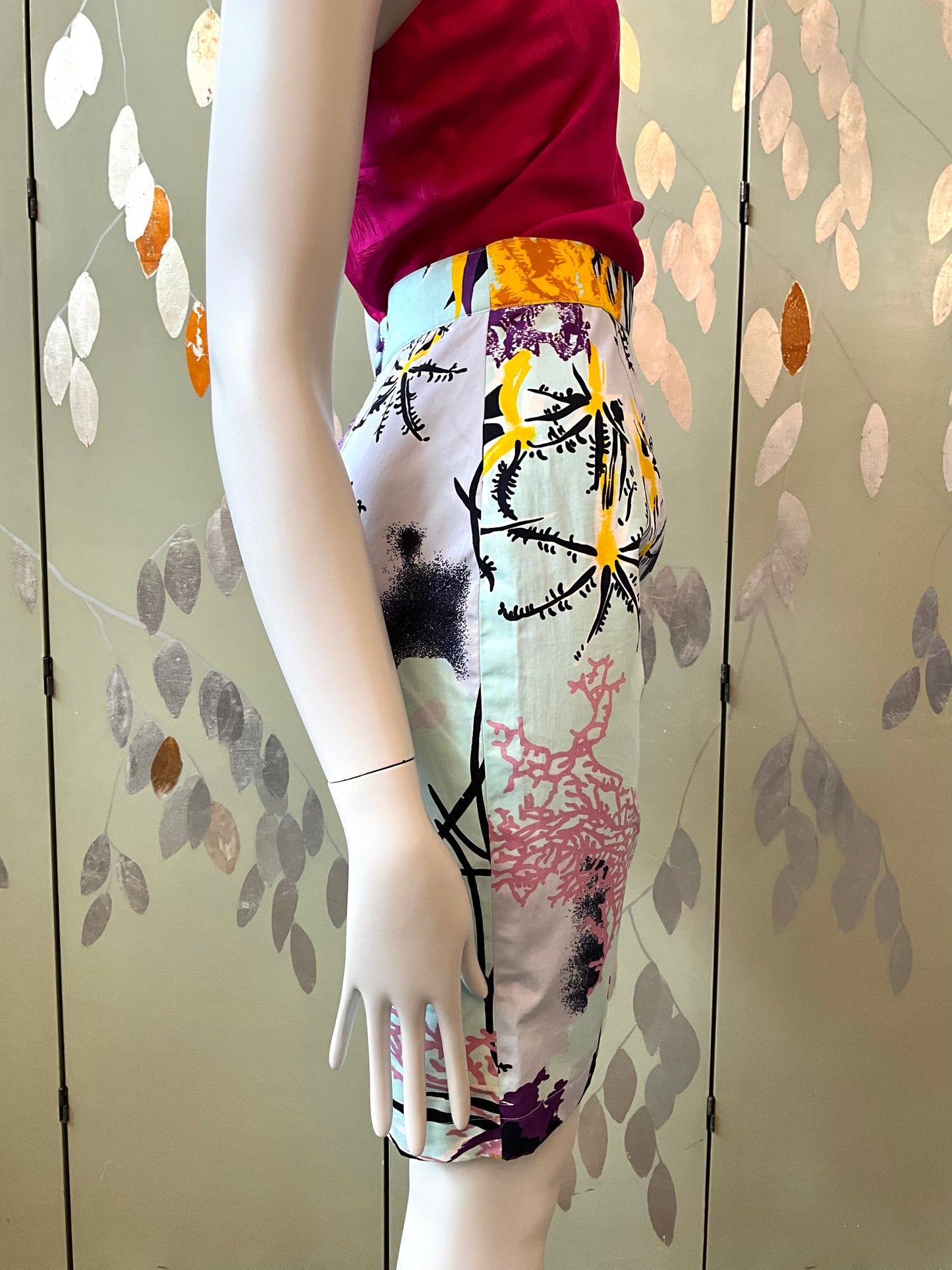 Mannequin wearing a colorful skirt with abstract patterns against a decorative wall.