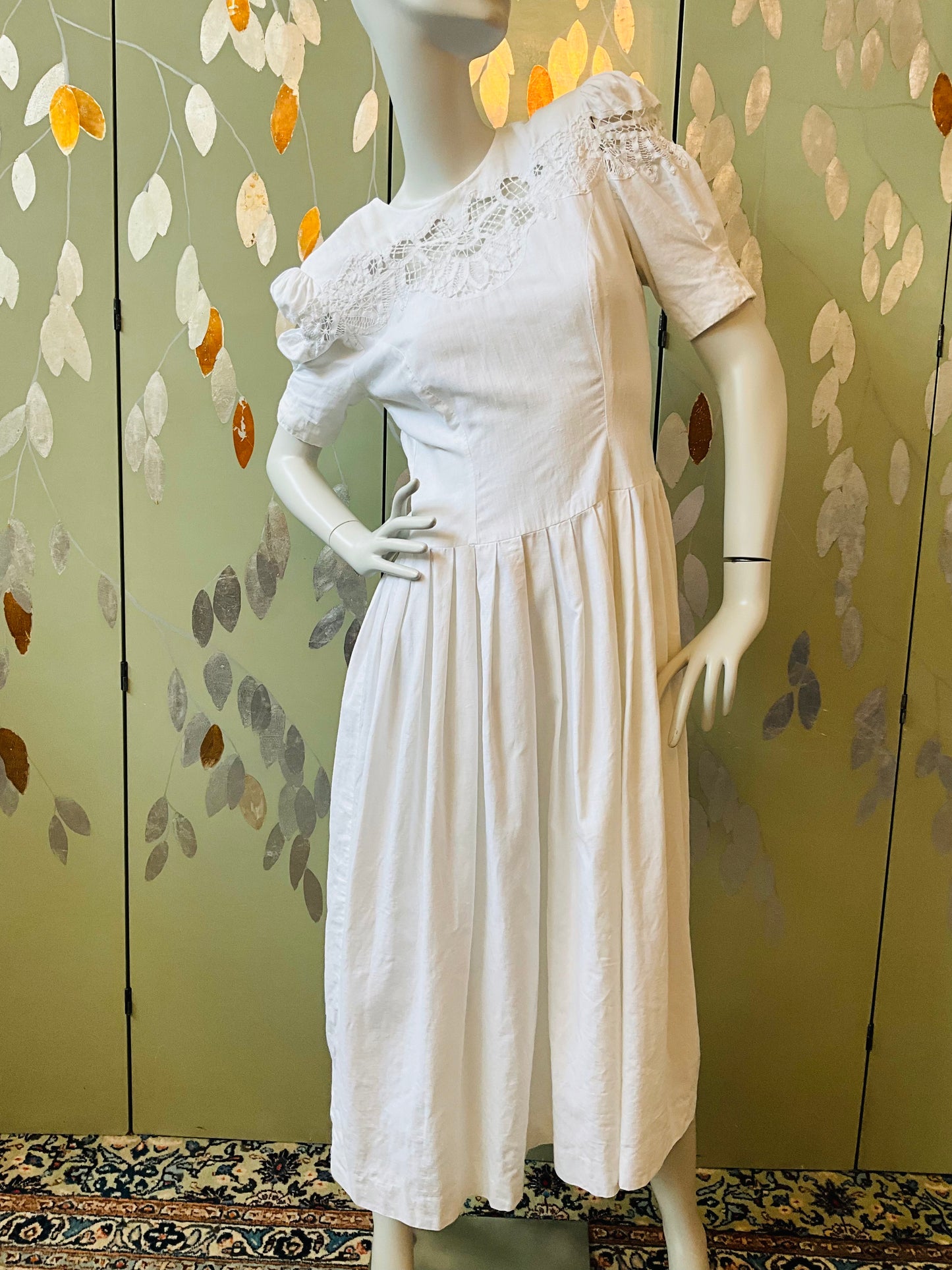 White dress on a mannequin against a decorative wall with leaf patterns.