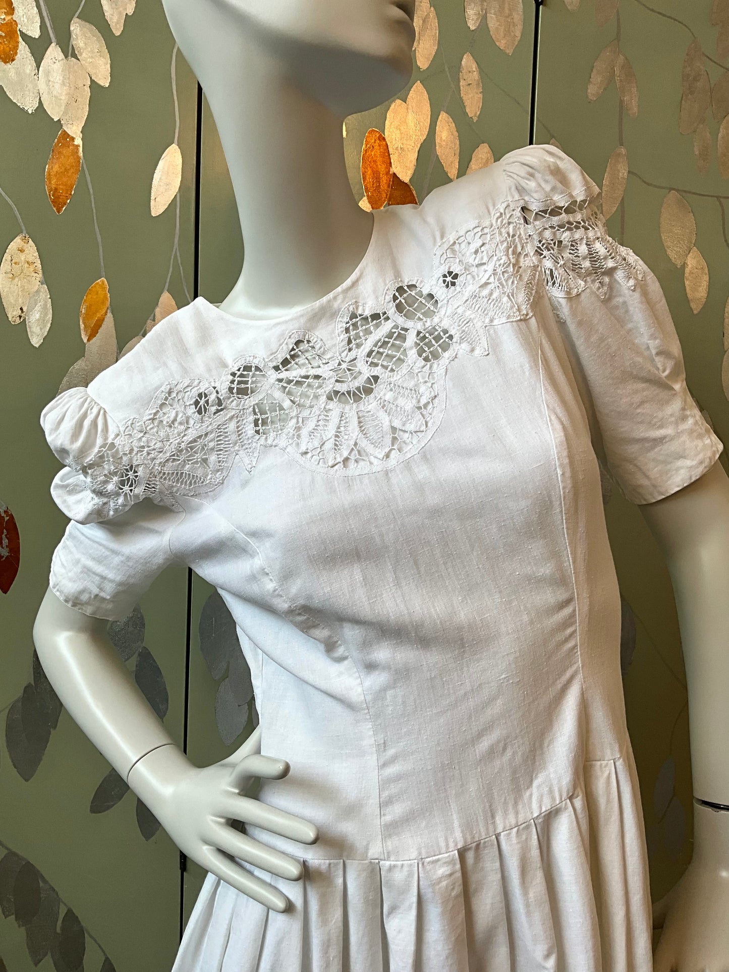White dress with lace details on a mannequin against a decorative wall.