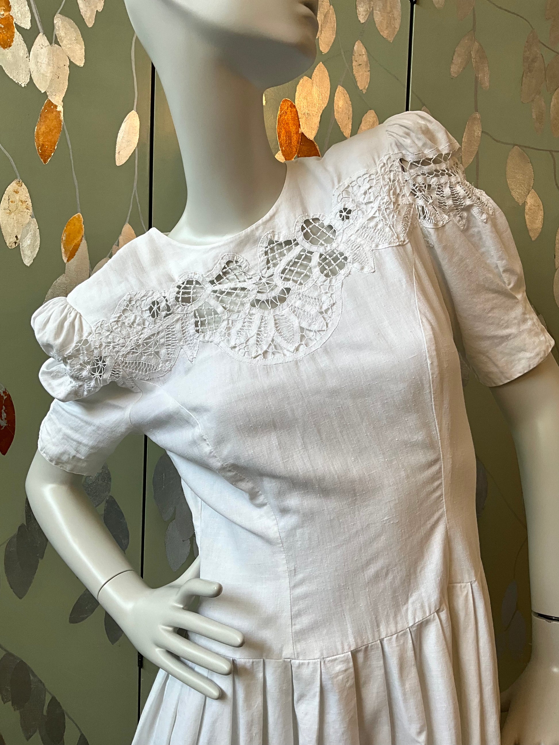 White dress with lace details on a mannequin against a decorative wall.