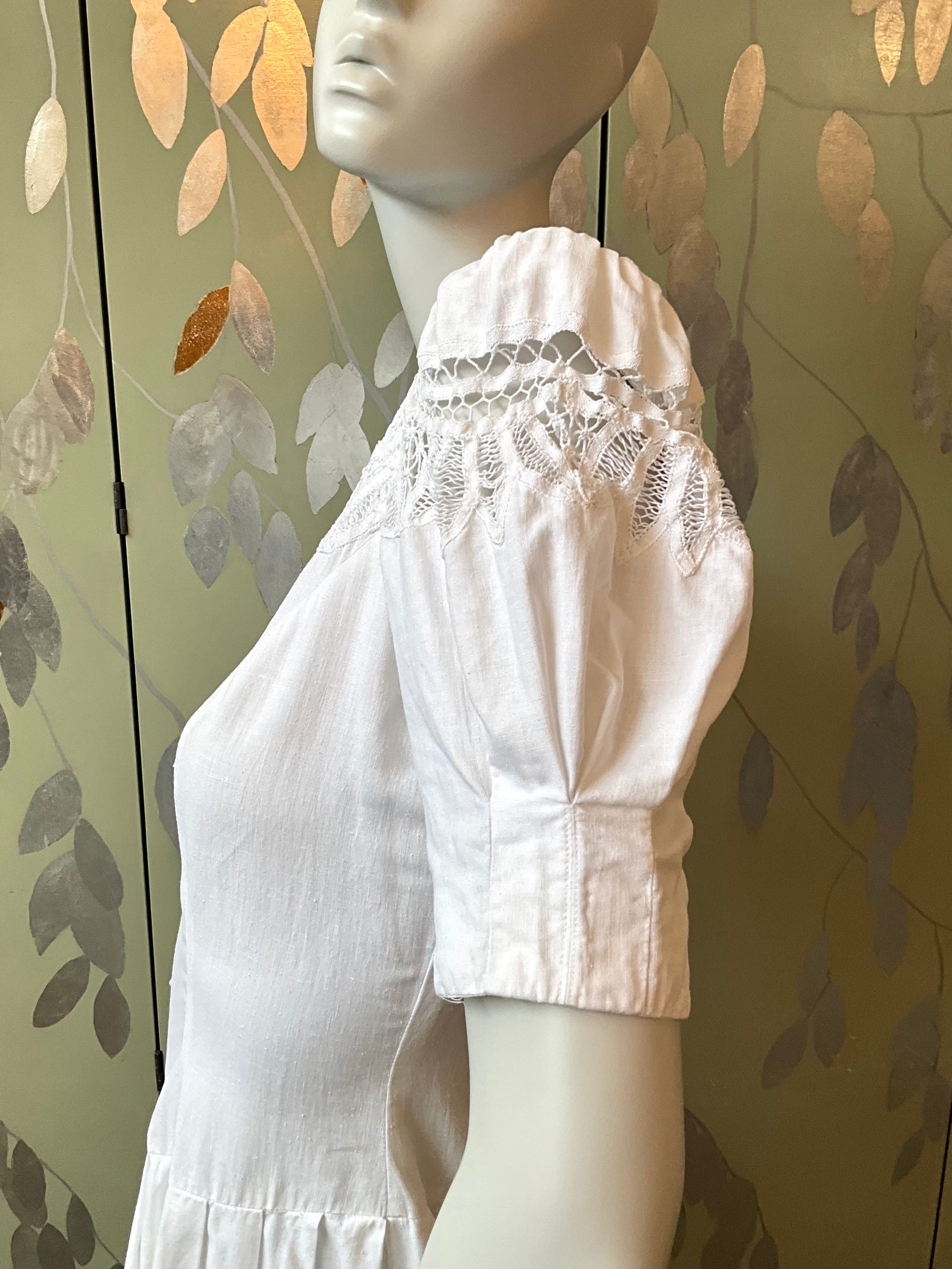 White lace dress on a mannequin against a leaf-patterned wall.