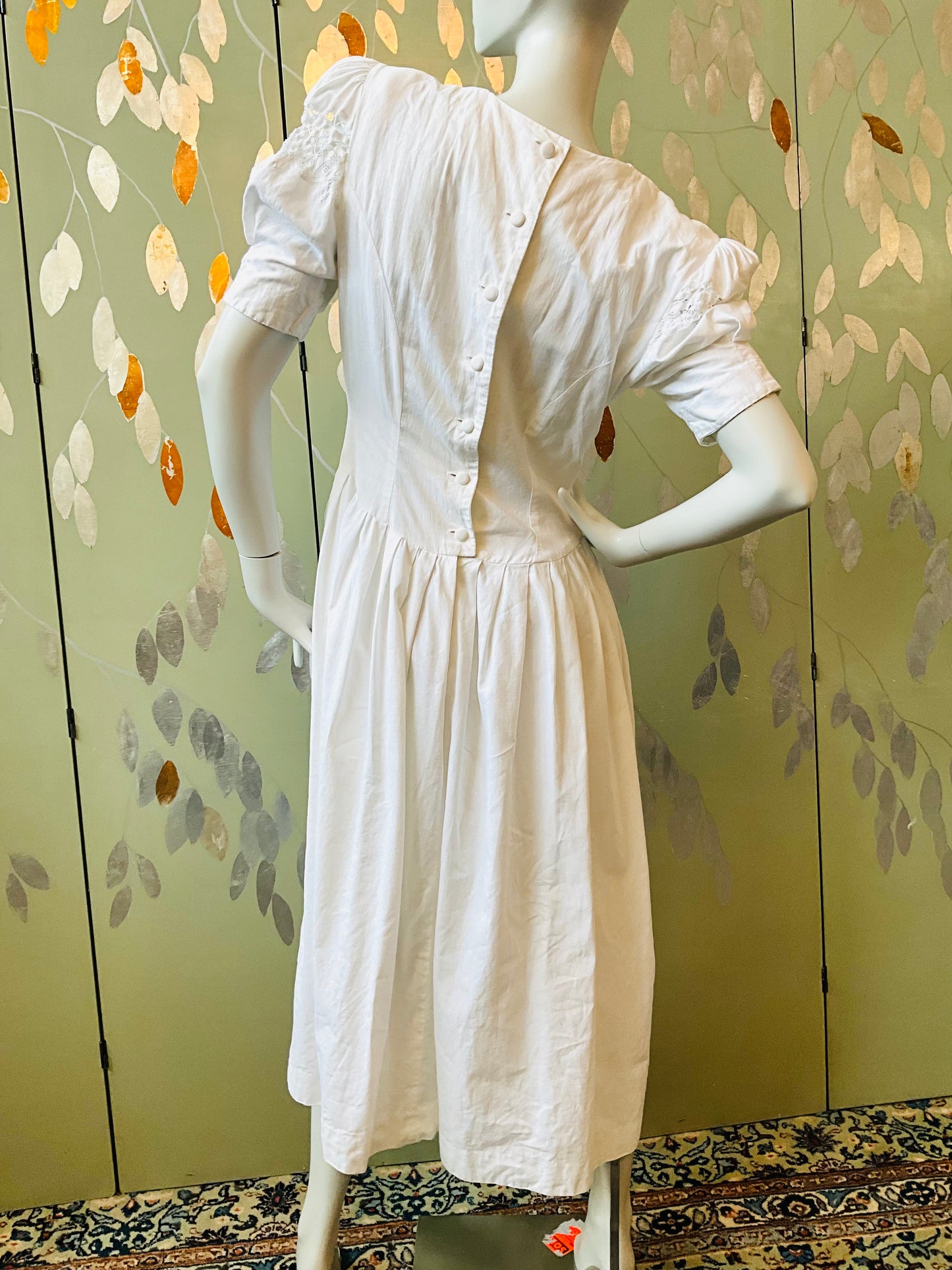 White dress on a mannequin against a floral-patterned wall.