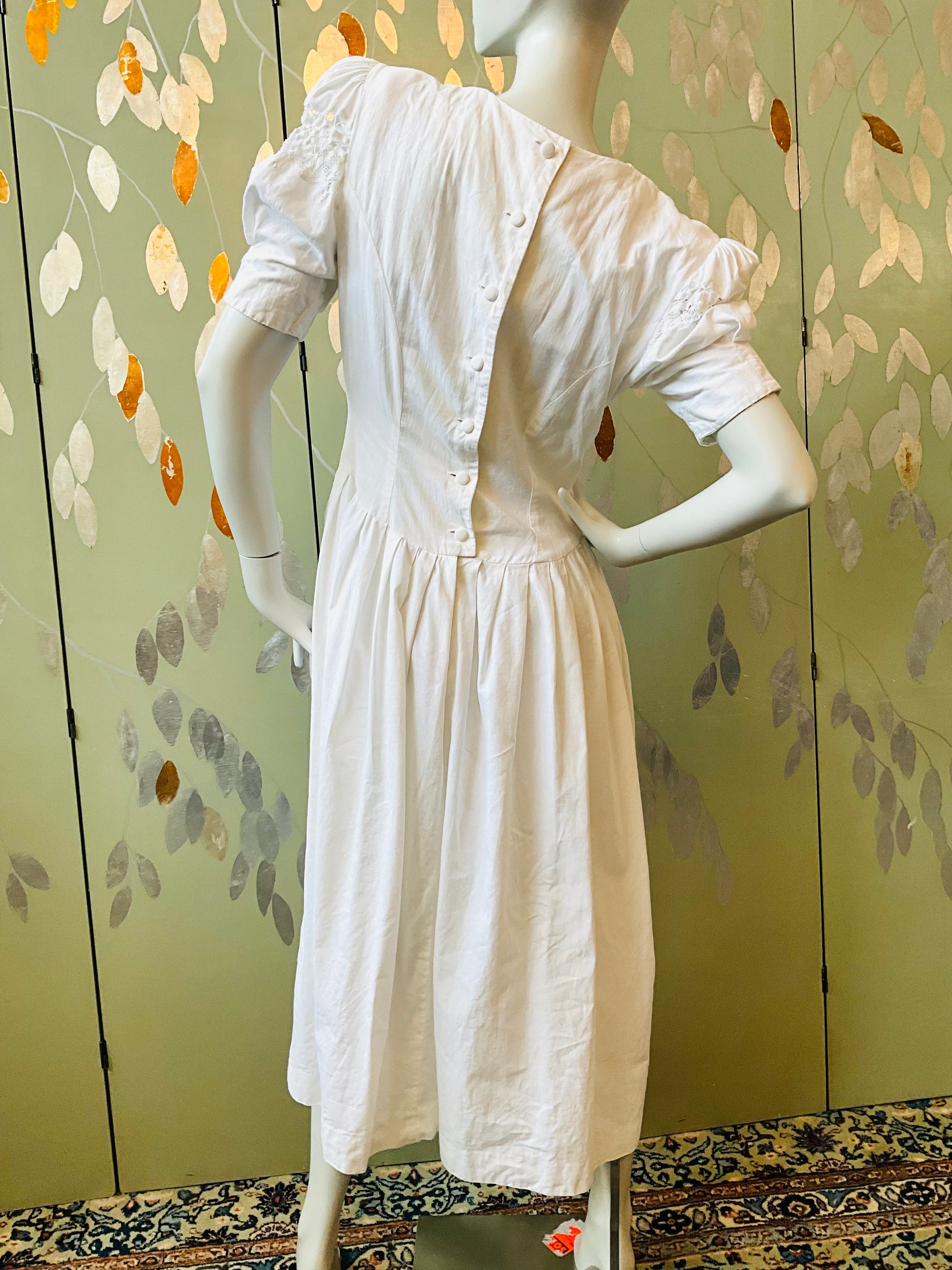 White dress on a mannequin against a floral-patterned wall.