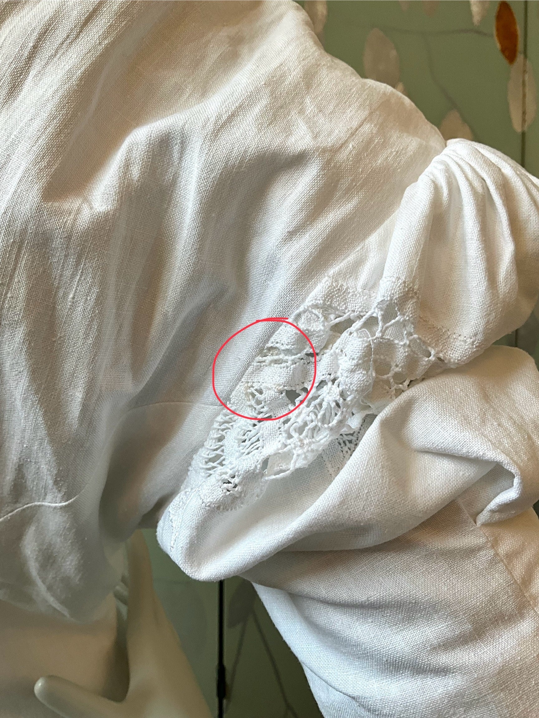 White blouse with lace detail on a mannequin, showing a red circle around a flaw.