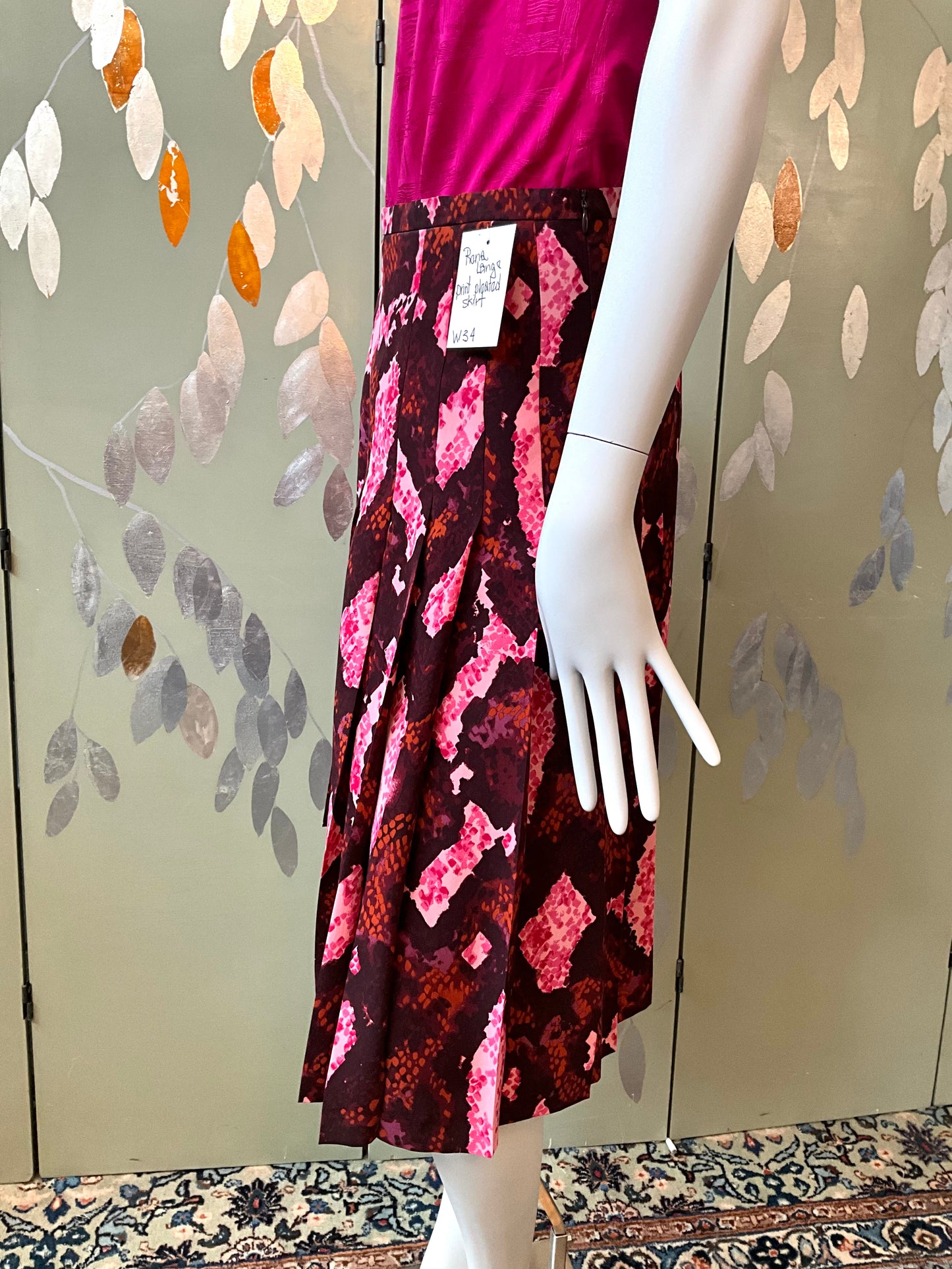 Mannequin wearing a patterned skirt with a pink top against a decorative wall.