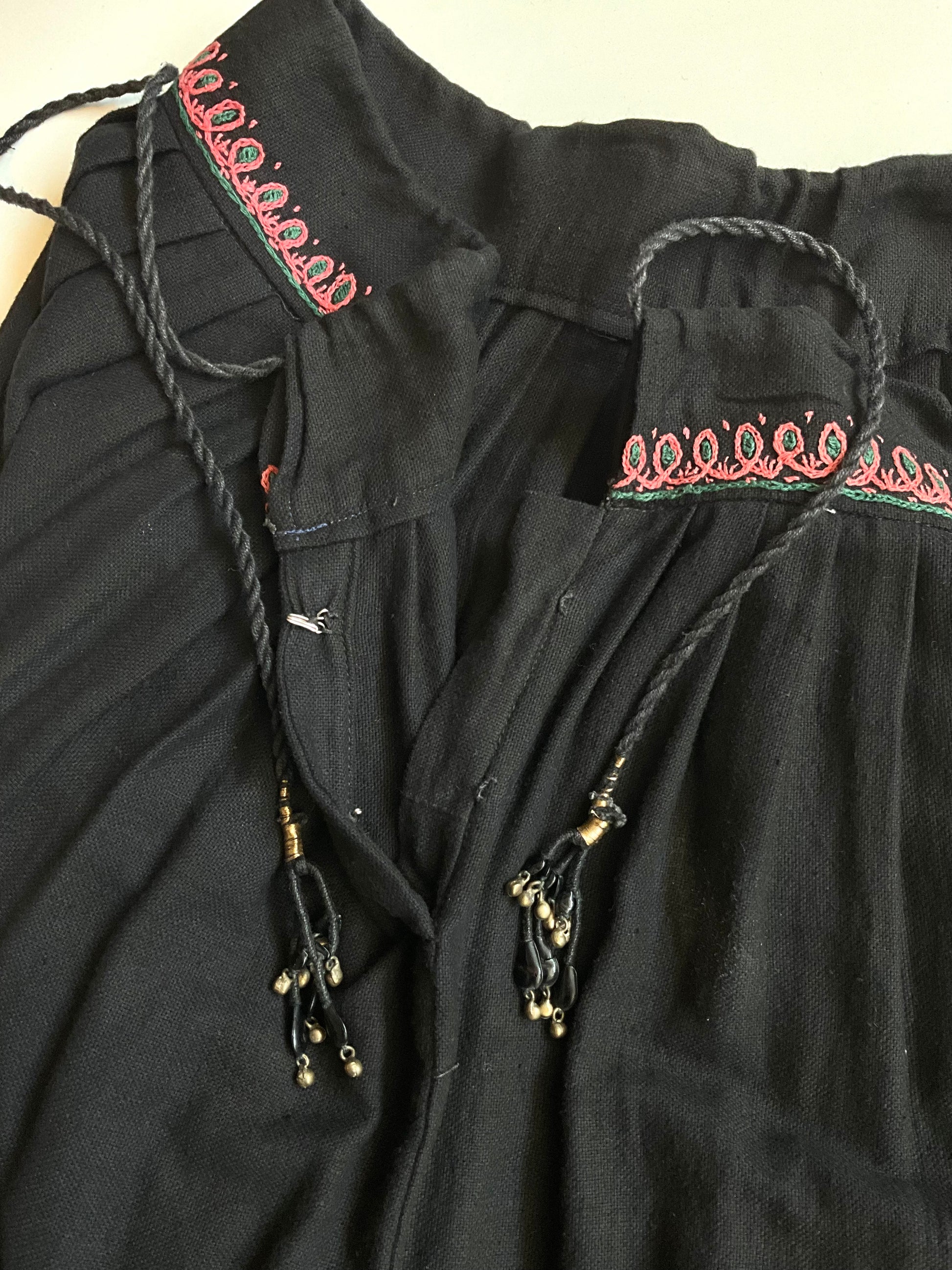 Black garment with intricate embroidery and tassels on a neutral background