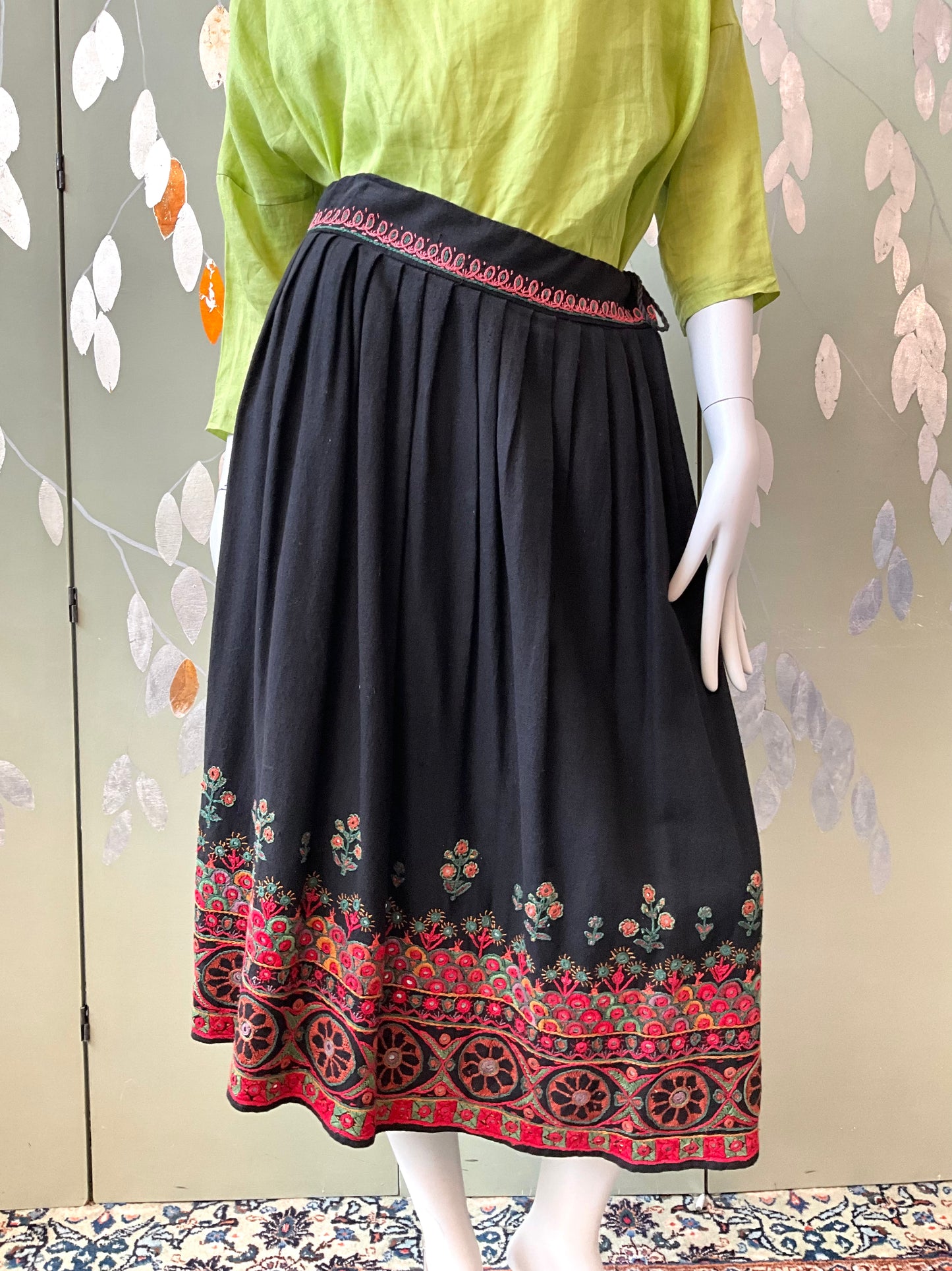 Black skirt with floral embroidery on a mannequin against a patterned background