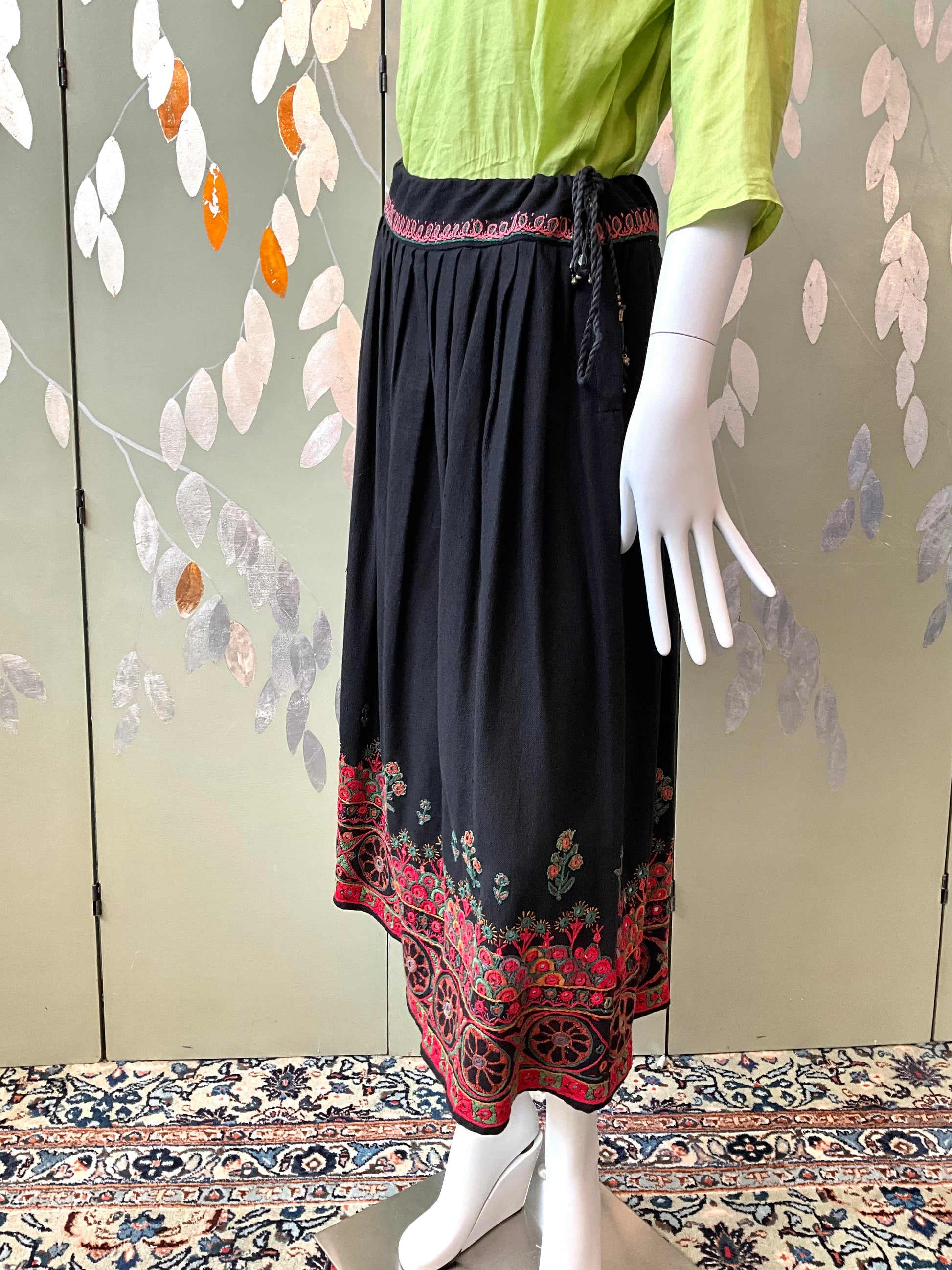 Mannequin wearing a green top and black skirt with red patterns on a decorative background