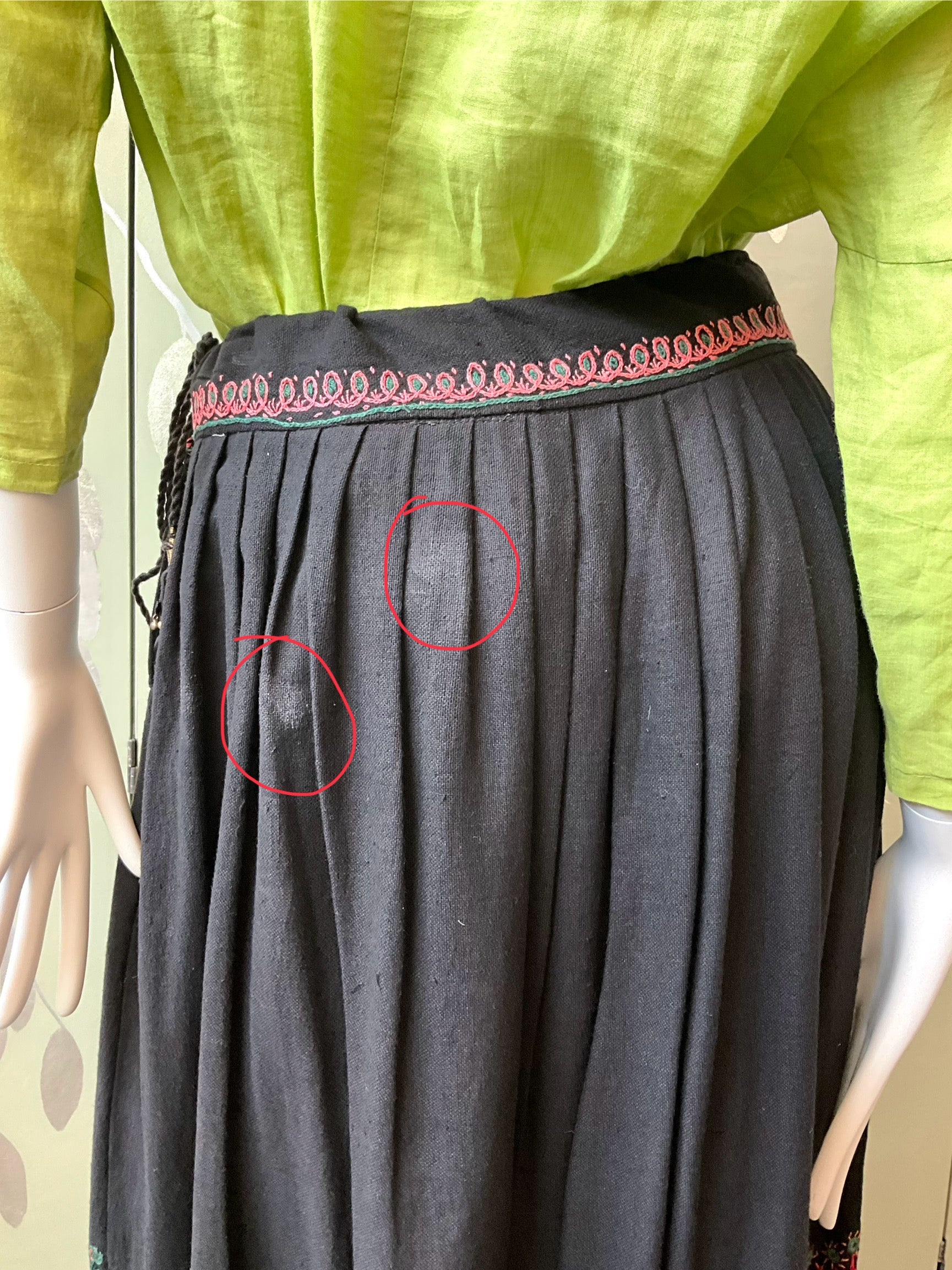 Mannequin wearing a green top and black skirt with red circles highlighting imperfections.