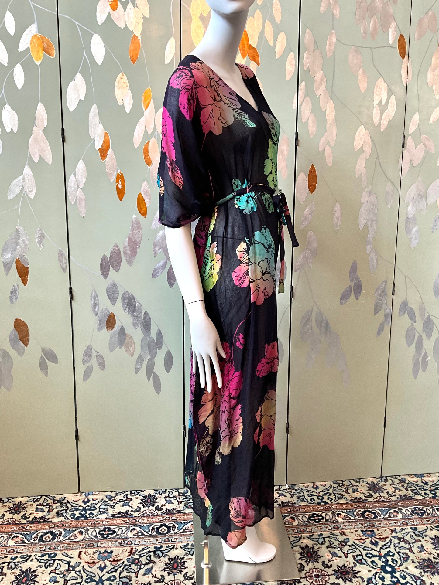 Mannequin wearing a black floral dress against a decorative wall.