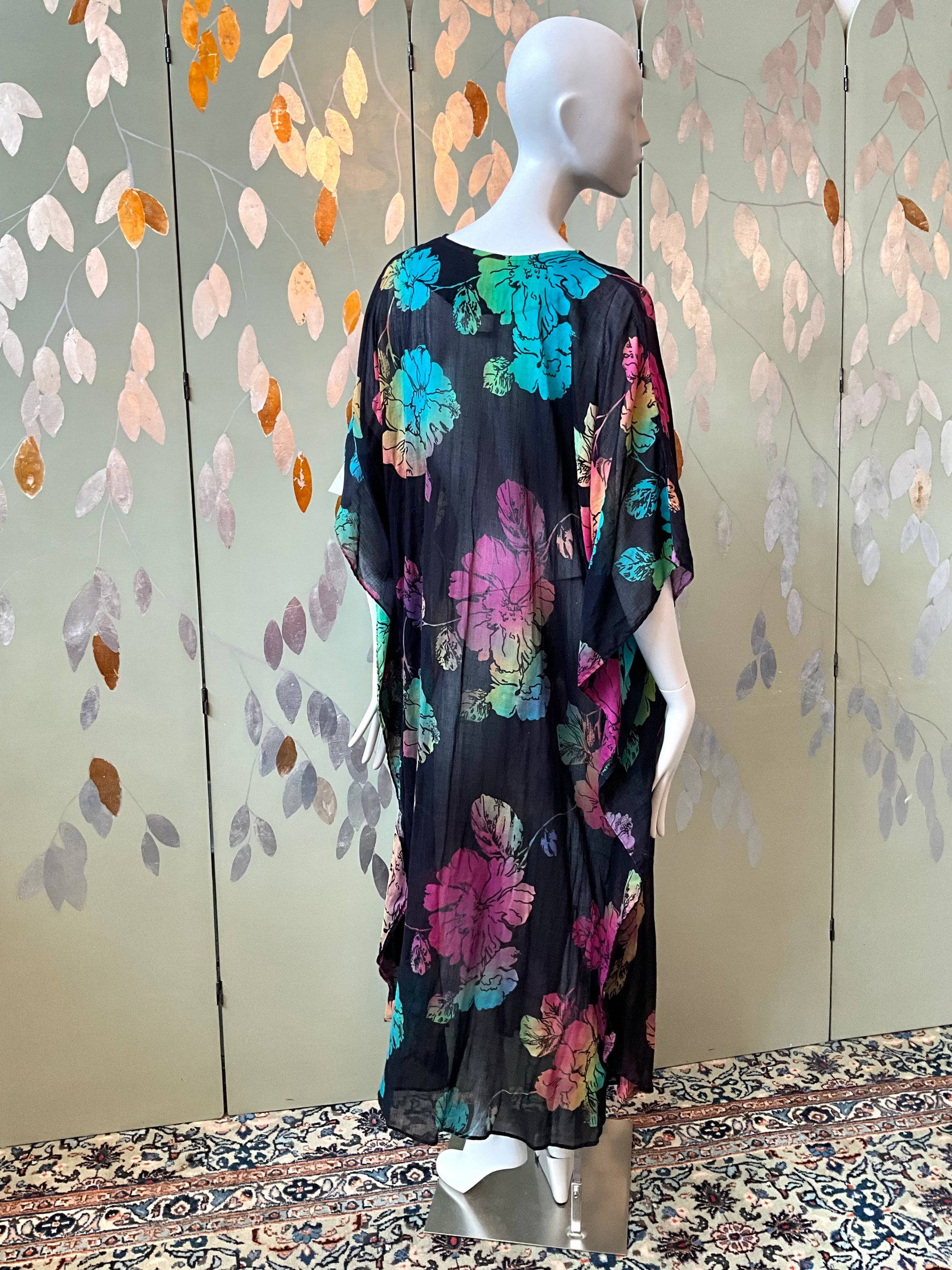 Mannequin wearing a black floral dress with a colorful pattern against a decorative wall.
