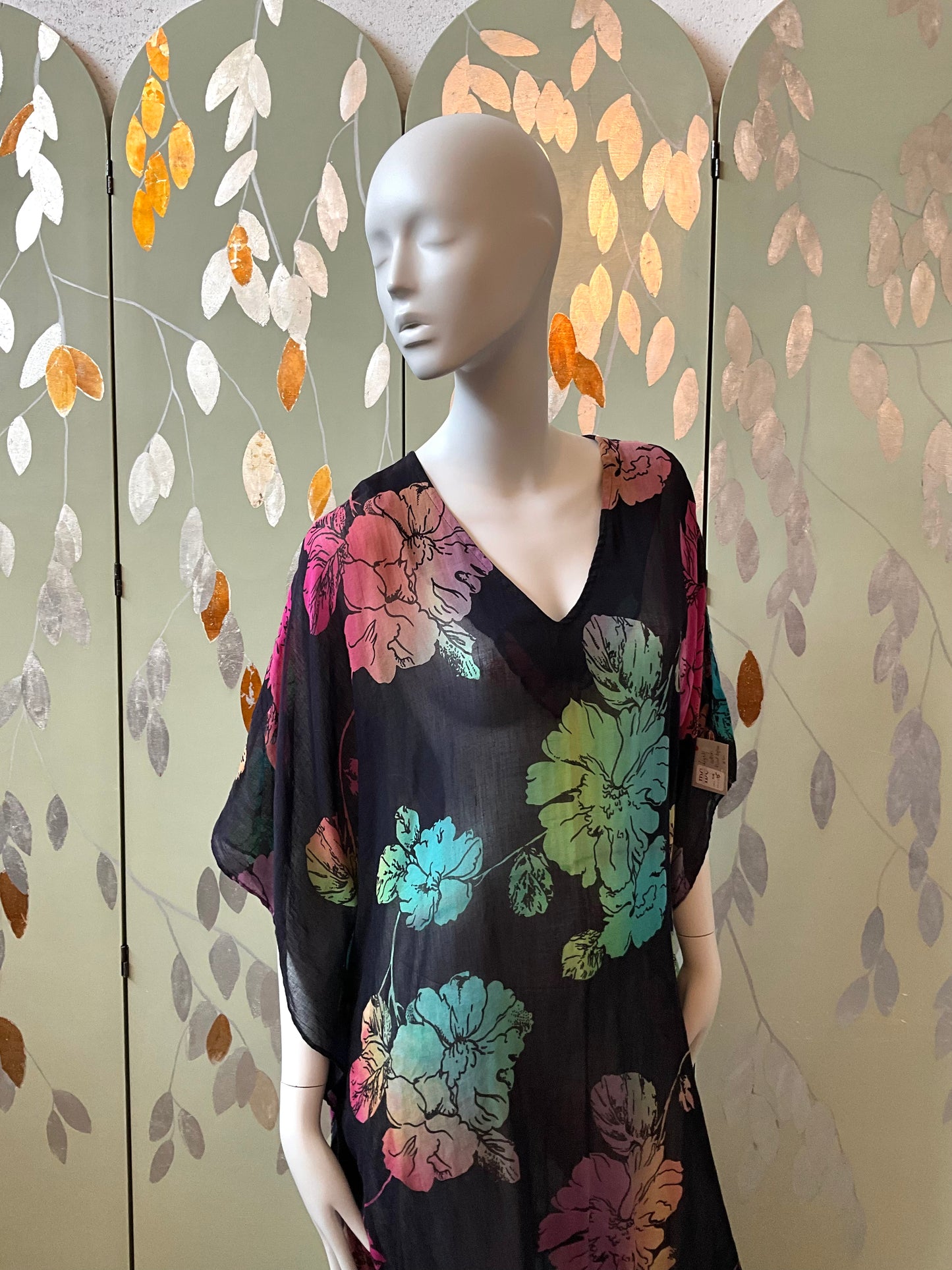 Mannequin wearing a black floral dress against a decorative wall with leaf patterns.
