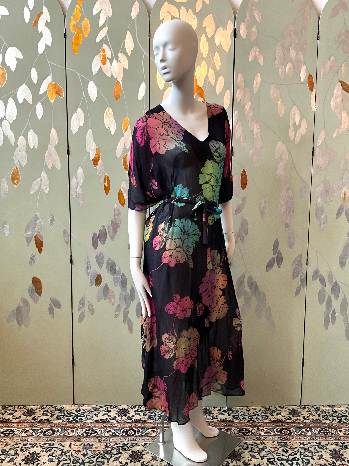 Mannequin wearing a black floral dress in front of a decorative wall with leaf patterns.