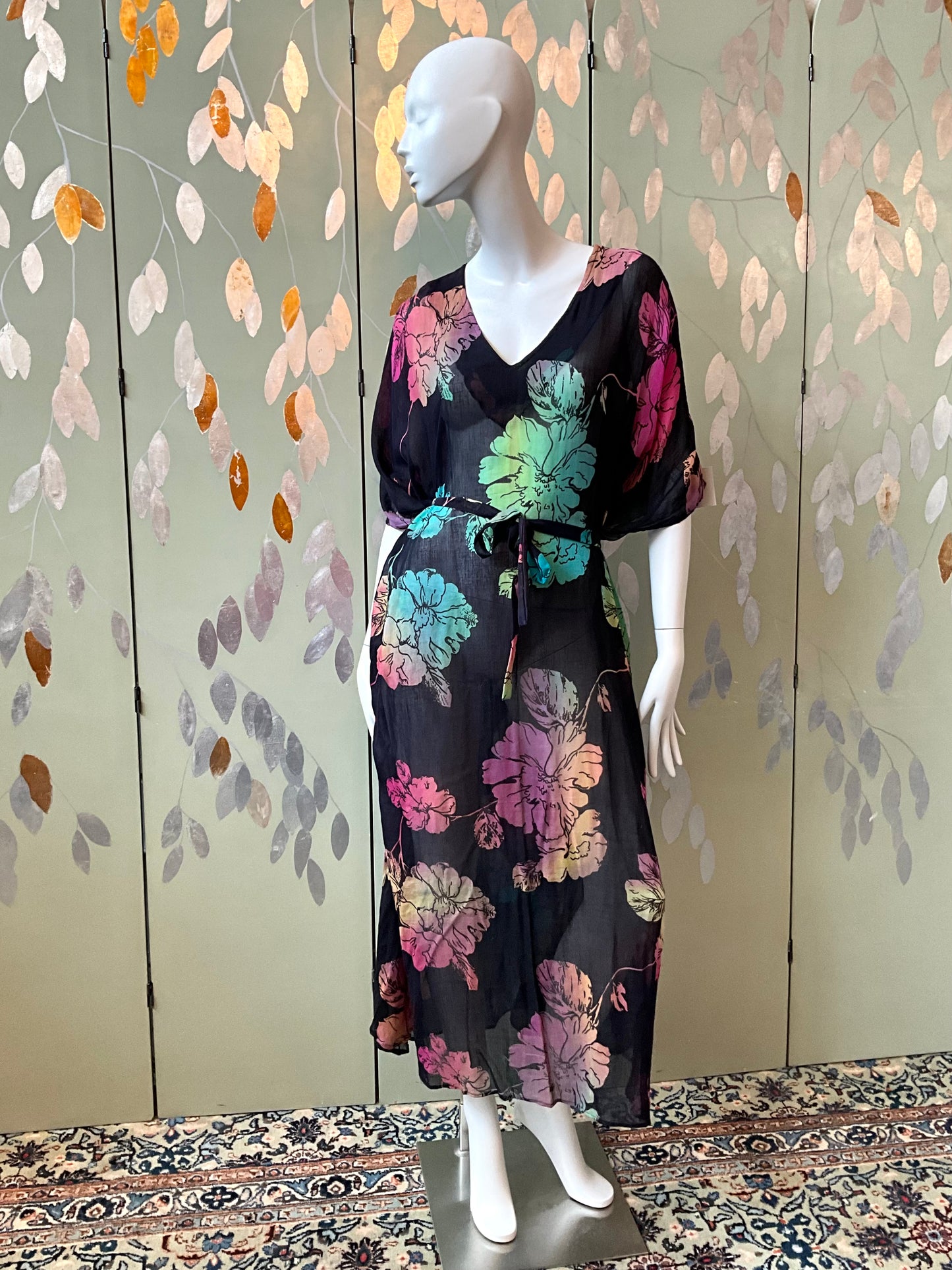 Mannequin wearing a black floral dress against a decorative wall.