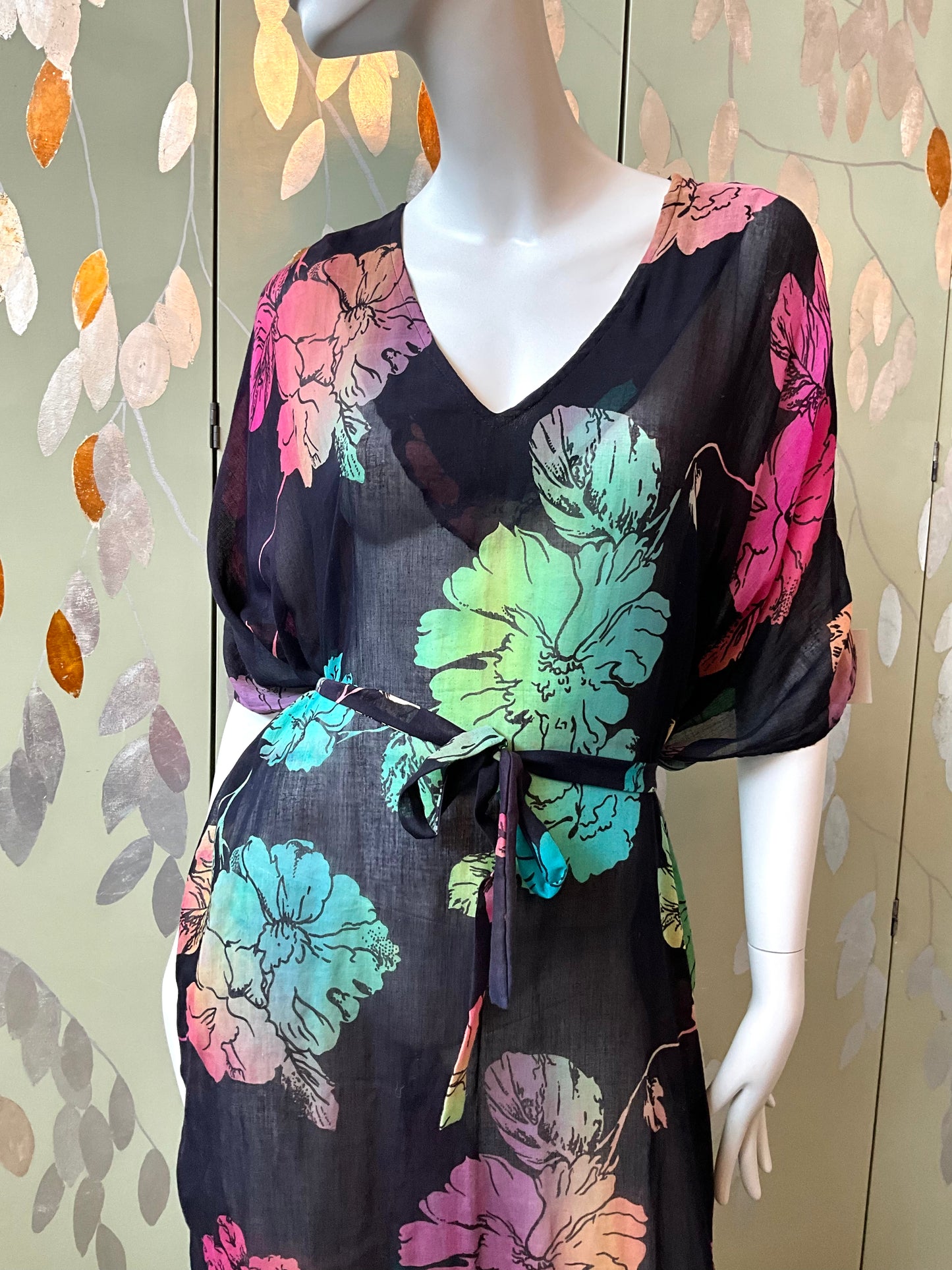 Mannequin wearing a black dress with colorful floral patterns against a decorative wall.