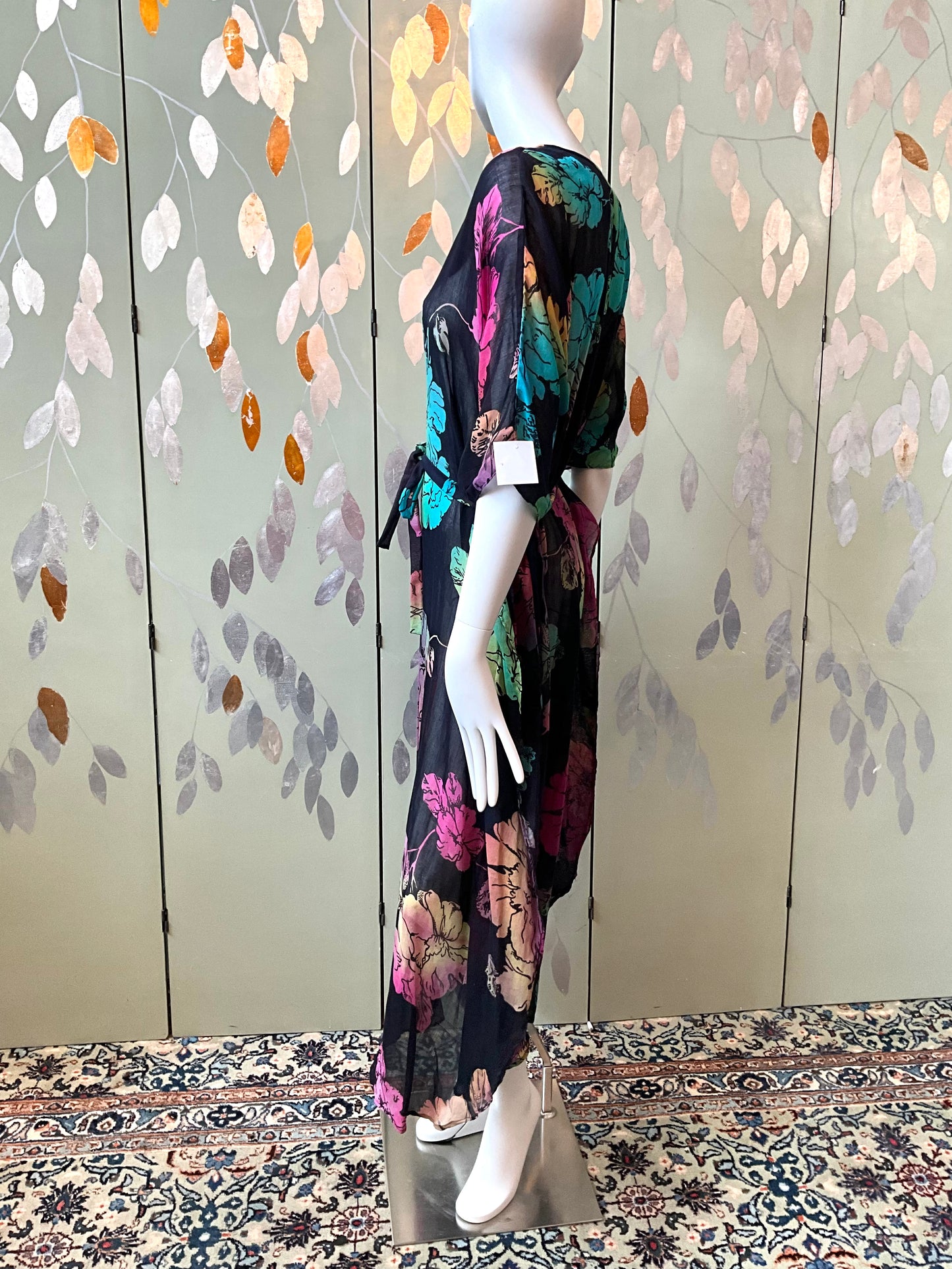 Mannequin wearing a floral dress against a decorative wall with leaf patterns.