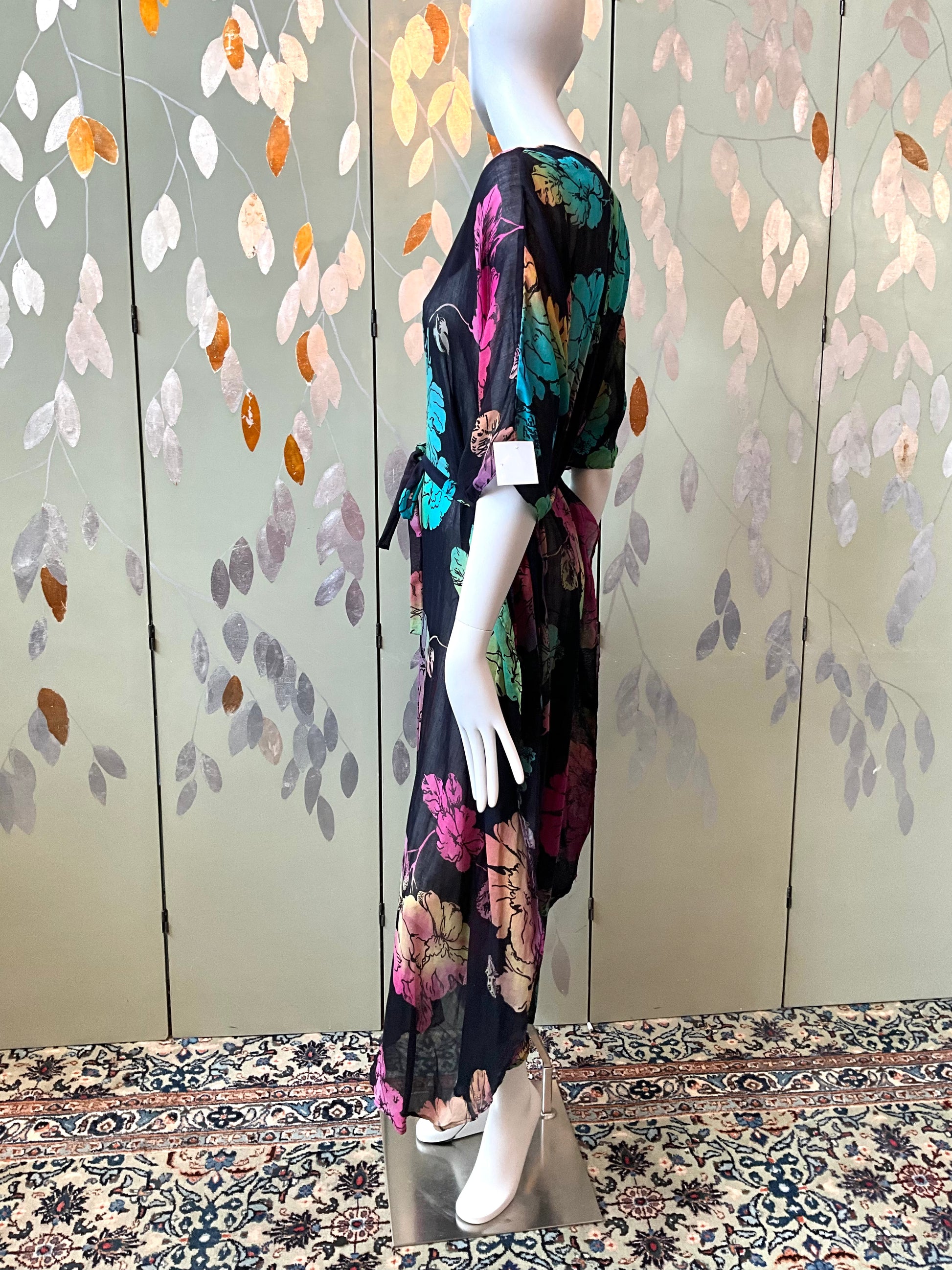 Mannequin wearing a floral dress against a decorative wall with leaf patterns.