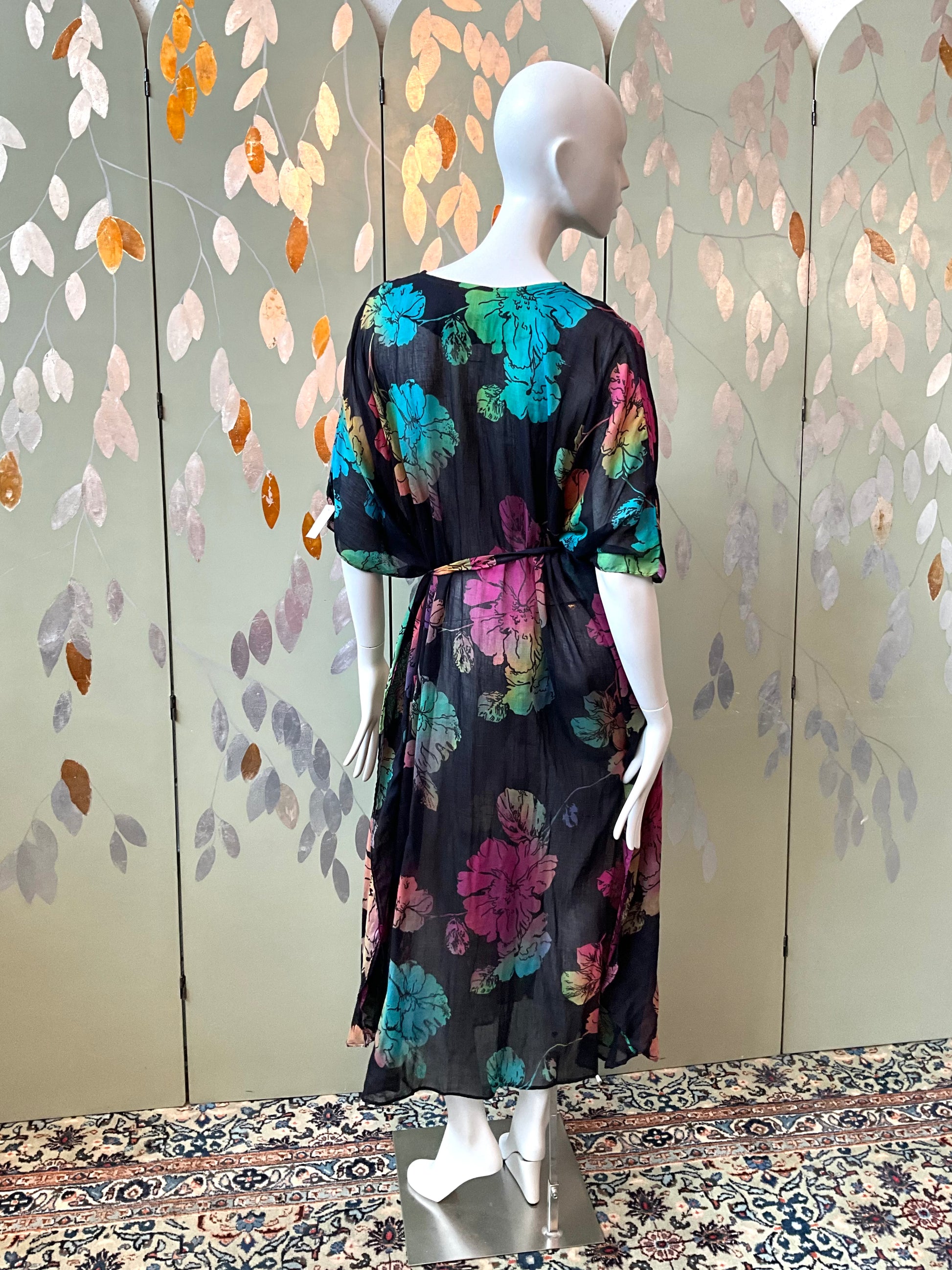 Mannequin wearing a black floral dress against a decorative wall.